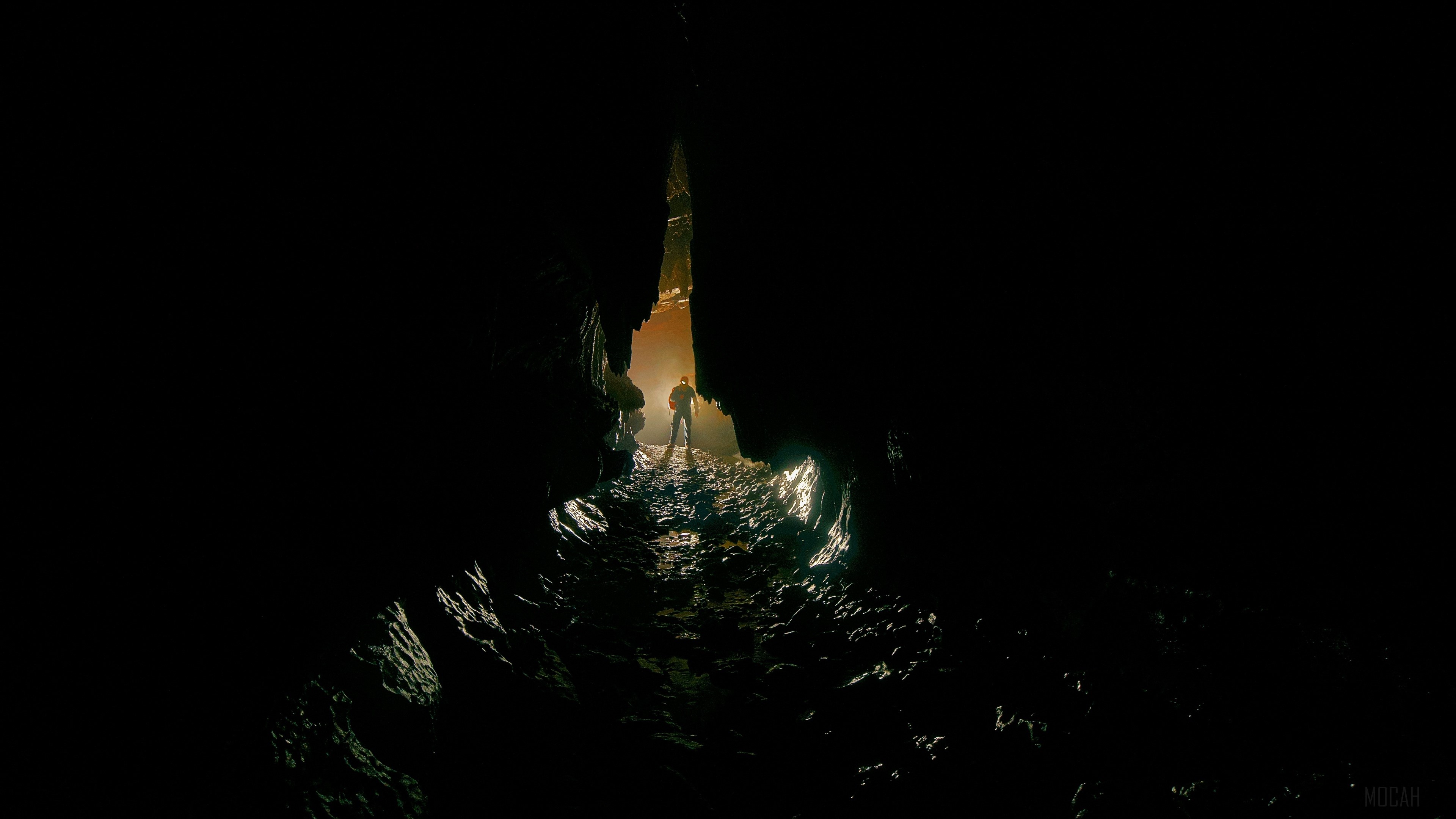 Man standing in a dark cave with light ahead 4K HD Wallpaper