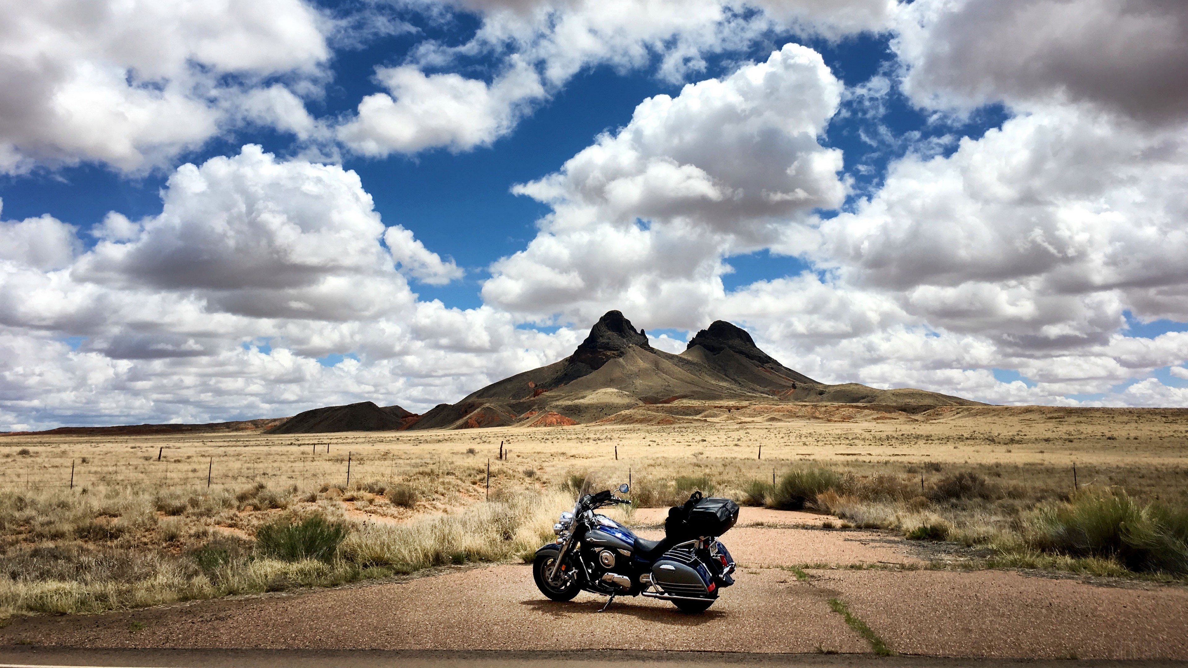 Motorcycle parked on road with mountains and clouds HD Wallpaper