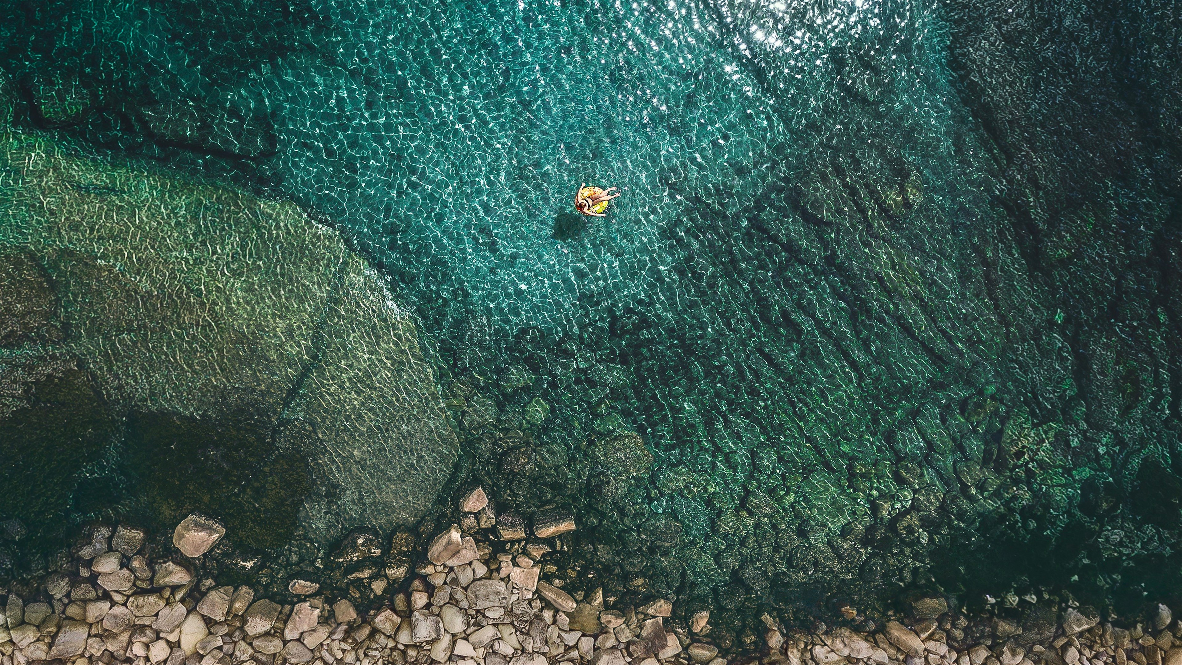 Person on inflatable in clear turquoise water HD Wallpaper