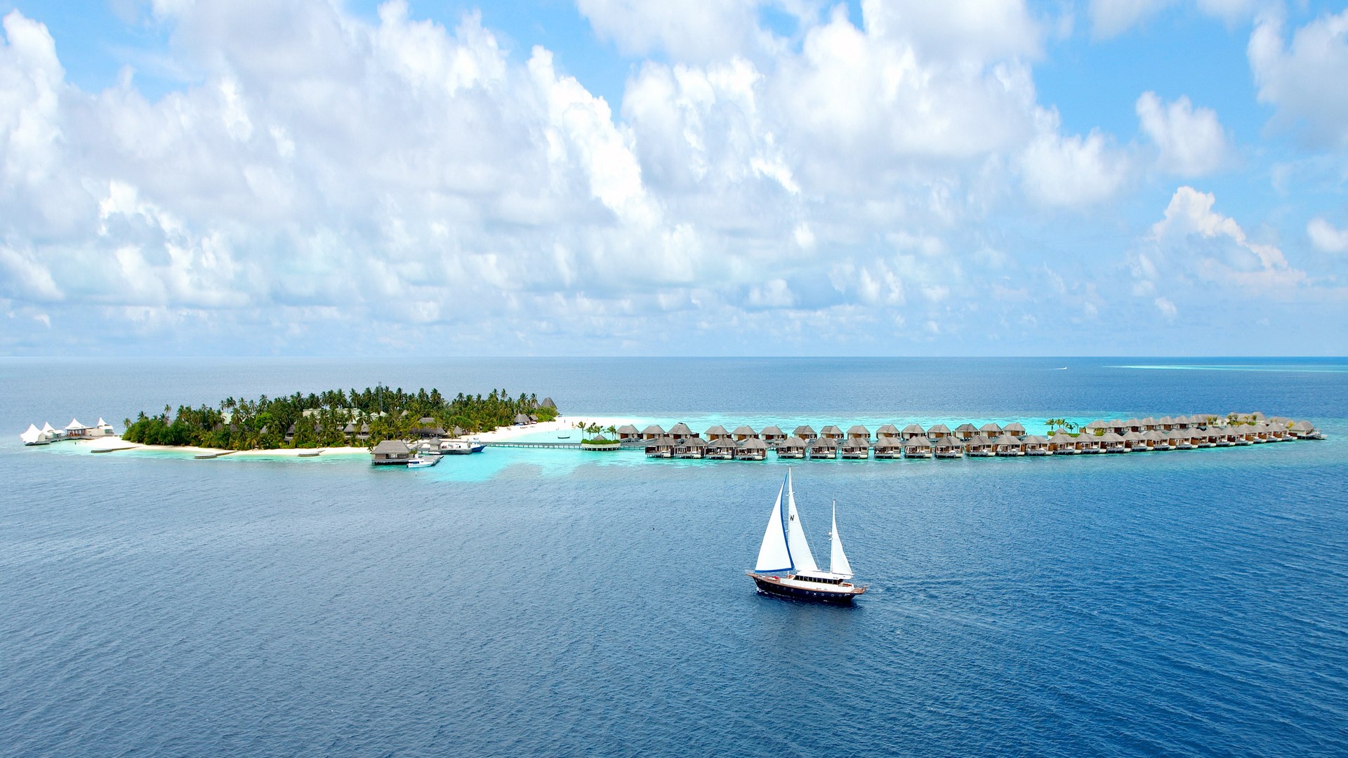 Sailboat near a tropical island resort with overwater bungalows HD Wallpaper