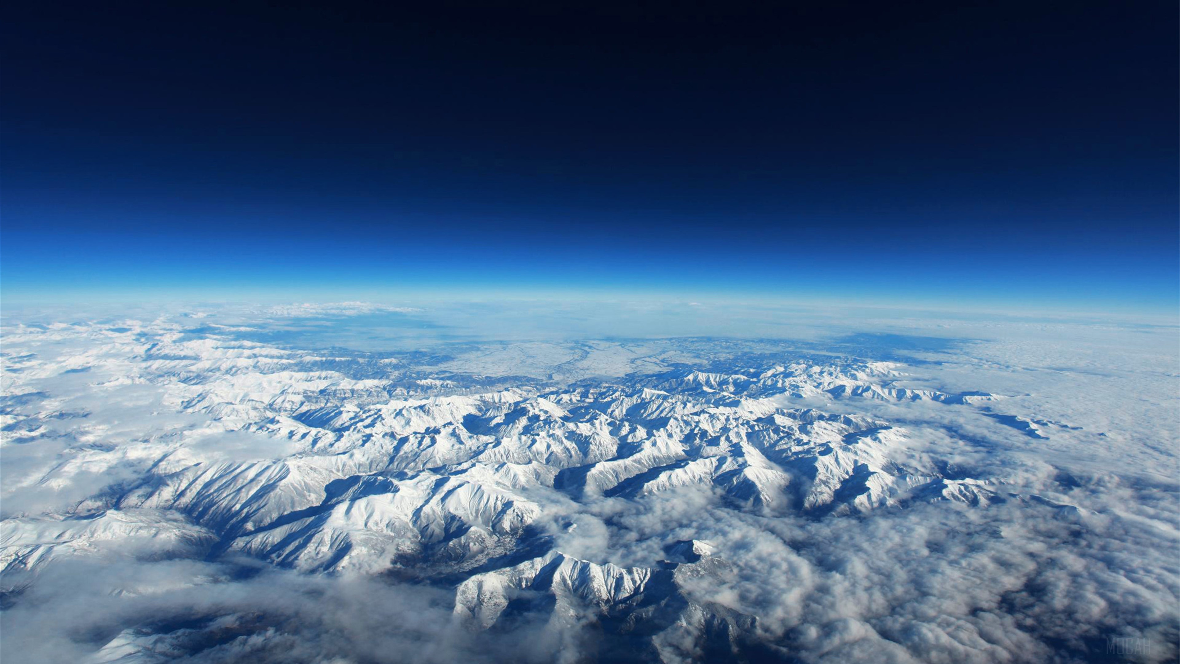 Aerial view of snow-covered mountains under a dark blue sky HD Wallpaper
