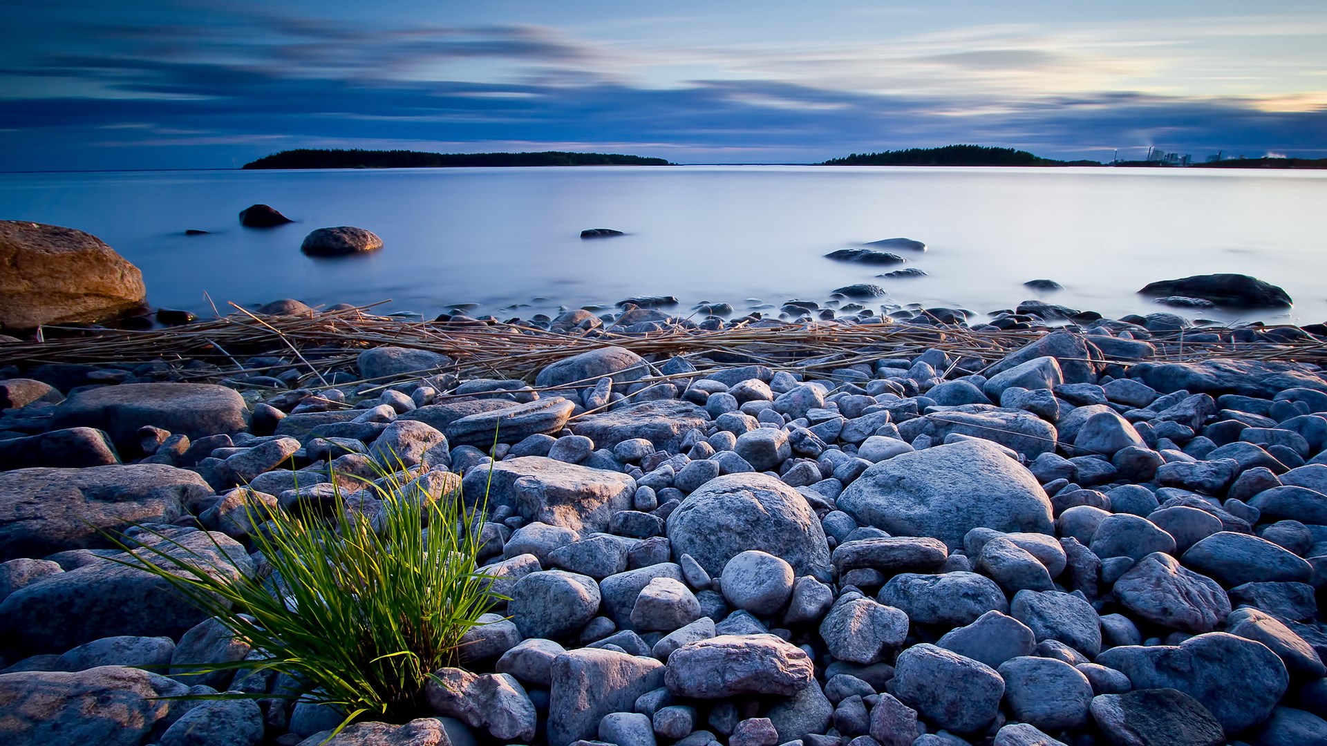 Rocky shore with calm water and distant islands at dusk HD Wallpaper