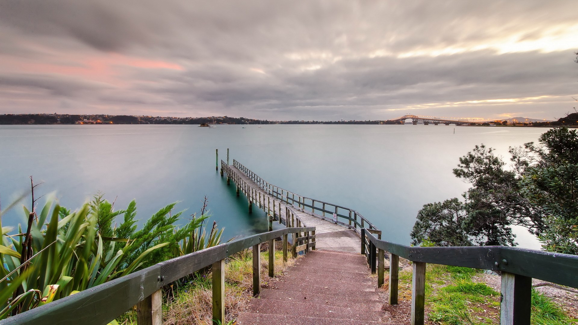Wooden pier extending into a calm bay at sunset HD Wallpaper