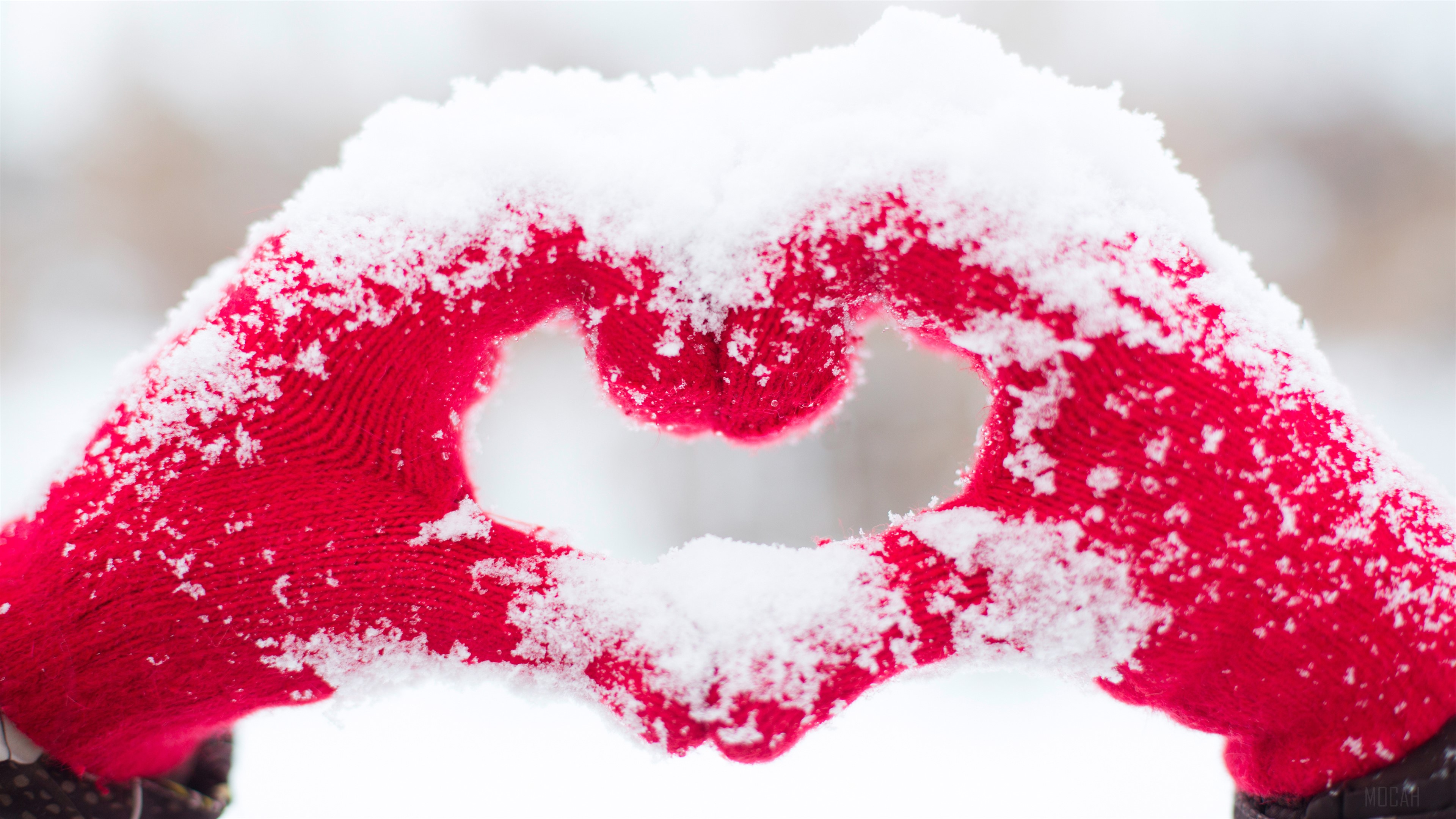 Hands in red gloves forming a heart shape in snow HD Wallpaper