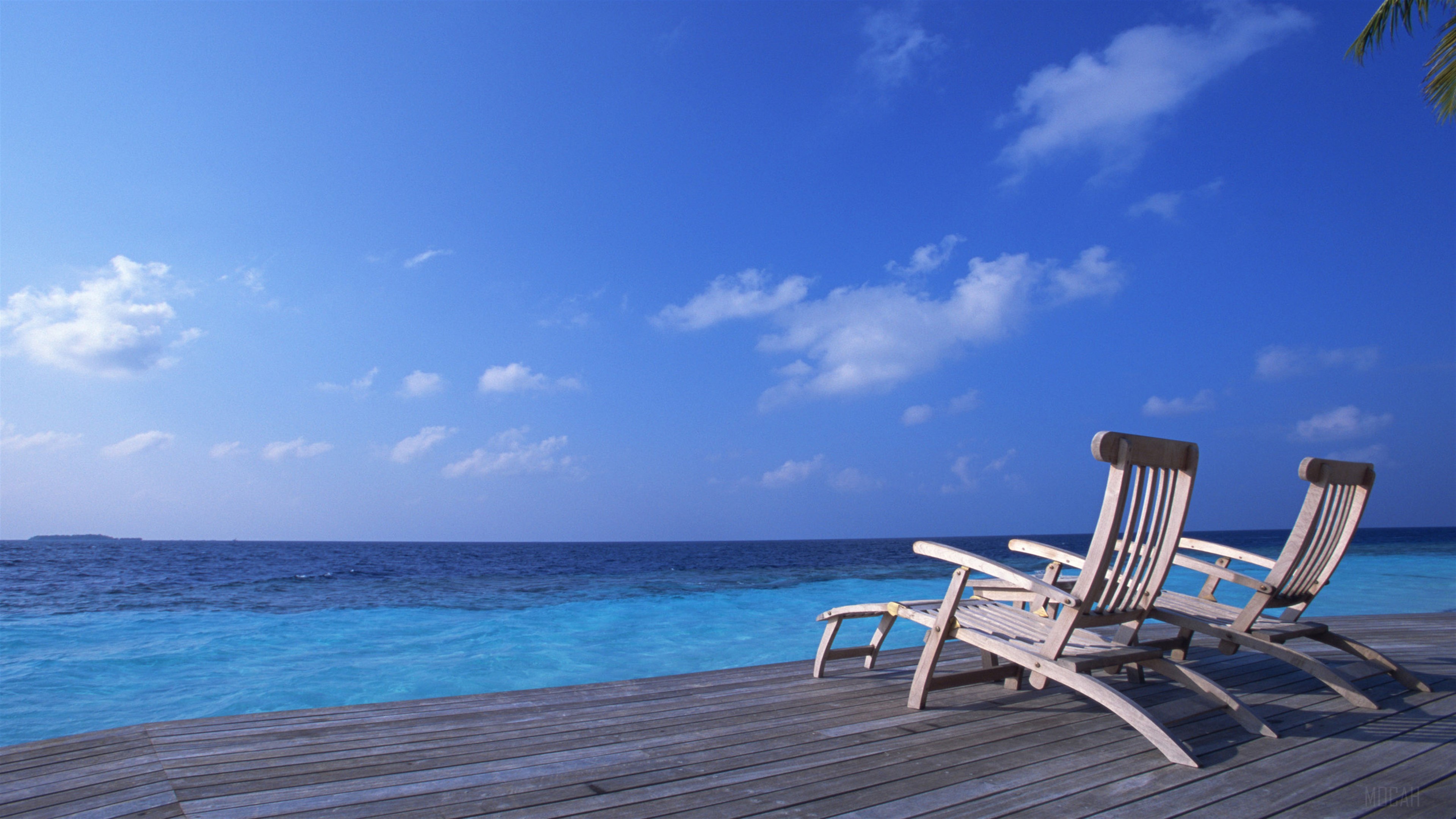 Two wooden lounge chairs on a deck overlooking the ocean HD Wallpaper