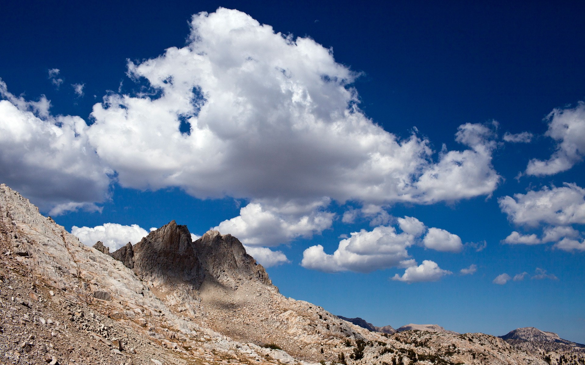Rocky mountain peaks under a cloudy blue sky HD Wallpaper