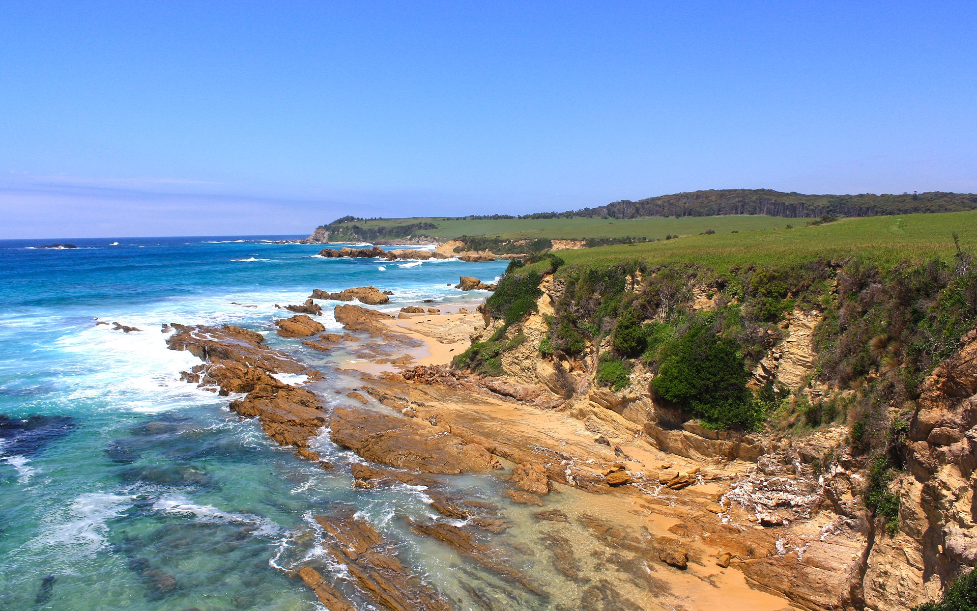 Rocky coastline with turquoise ocean and green hills HD Wallpaper