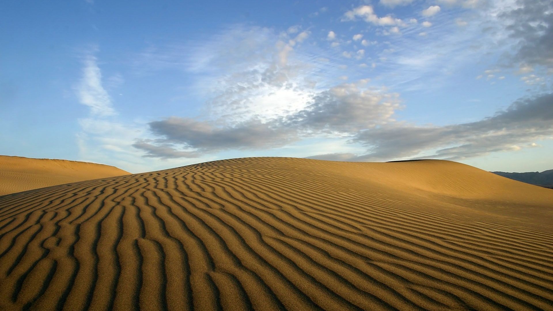 Sand dunes with rippled patterns under a cloudy sky HD Wallpaper