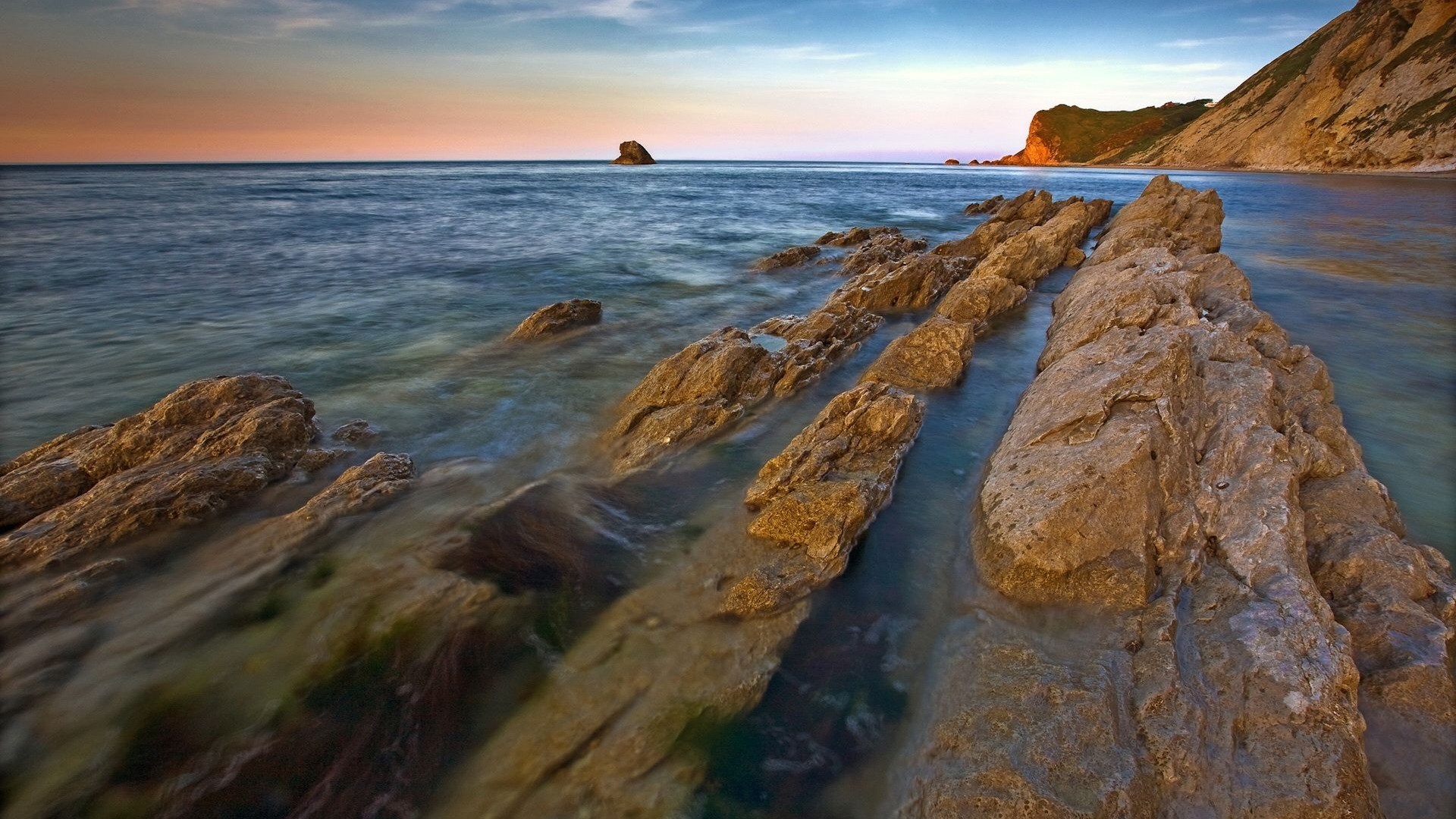 Rocky coastline at sunset with ocean waves HD Wallpaper