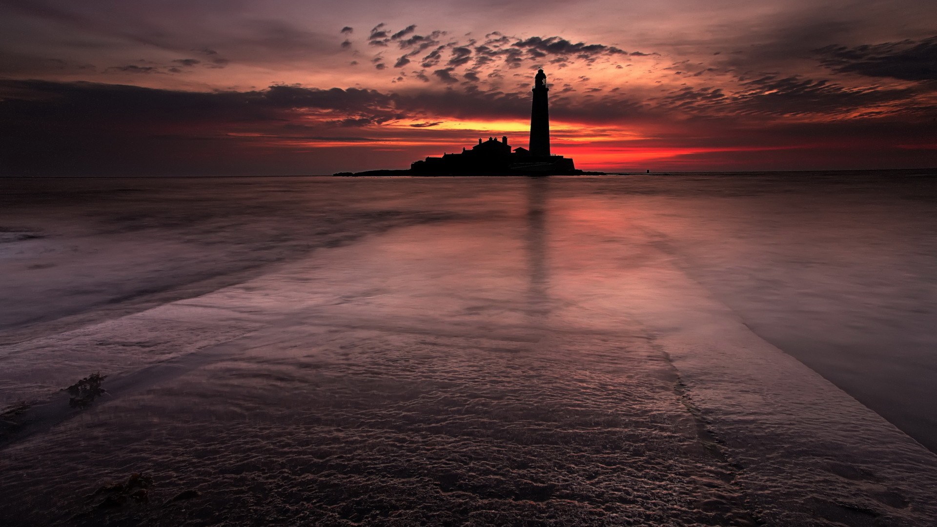 Silhouette of a lighthouse on an island at sunset HD Wallpaper