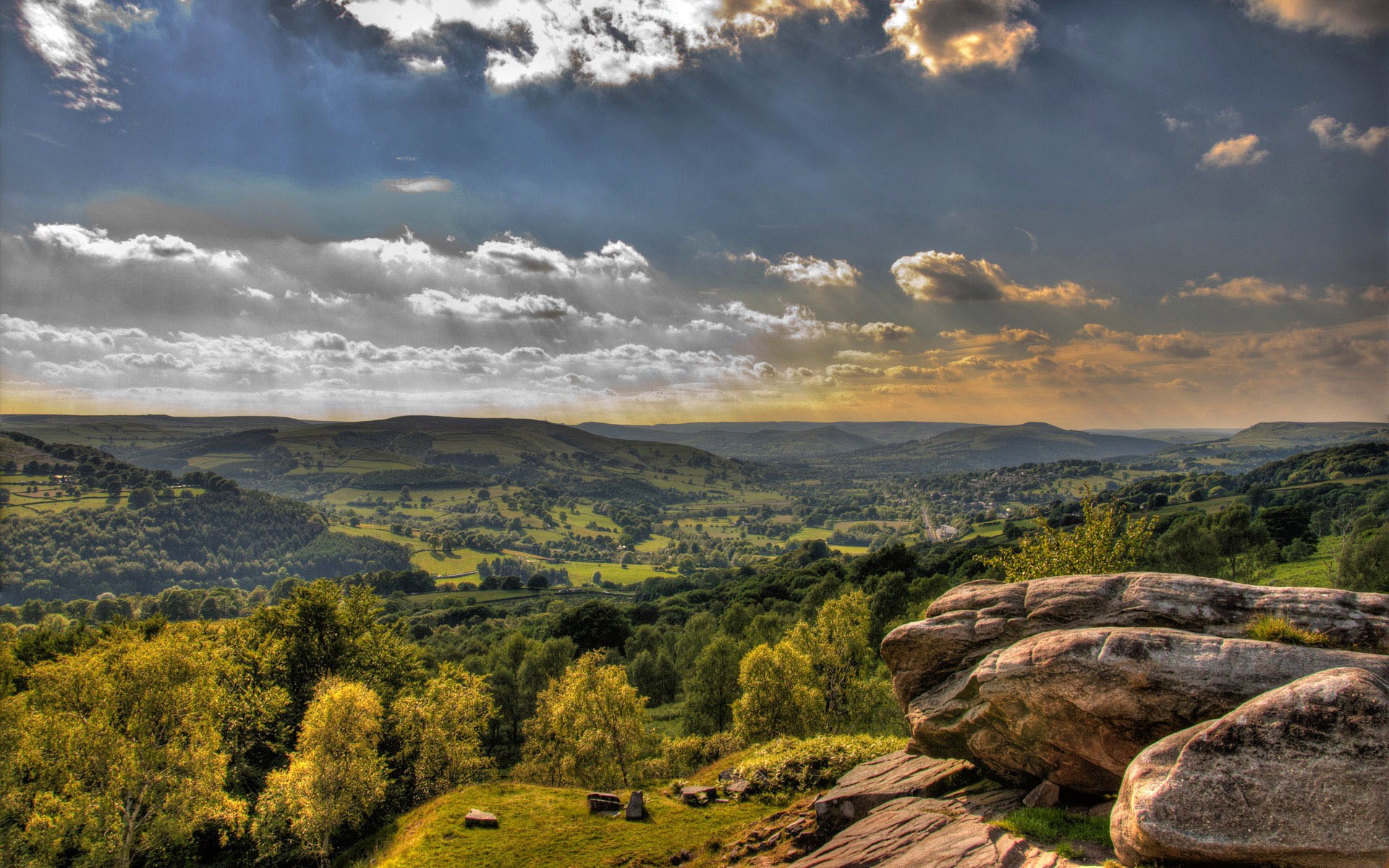Rocky outcrop overlooking a green valley under a cloudy sky HD Wallpaper