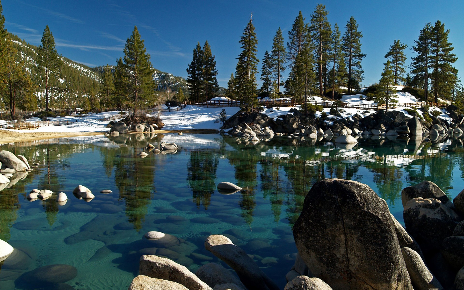 Clear lake with rocks and snow-covered trees HD Wallpaper