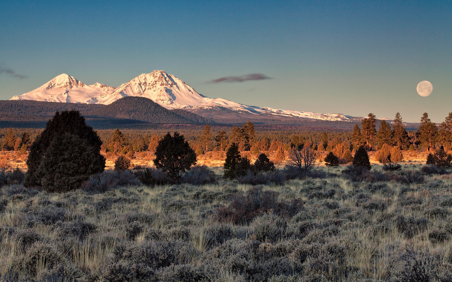 Snow-capped mountains and moon over a dry landscape HD Wallpaper