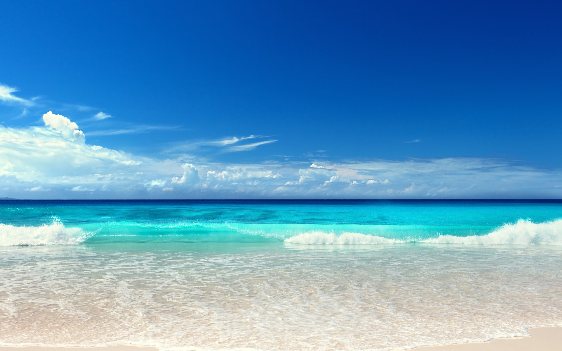 Turquoise ocean waves crash on a sandy beach under a blue sky. HD Wallpaper