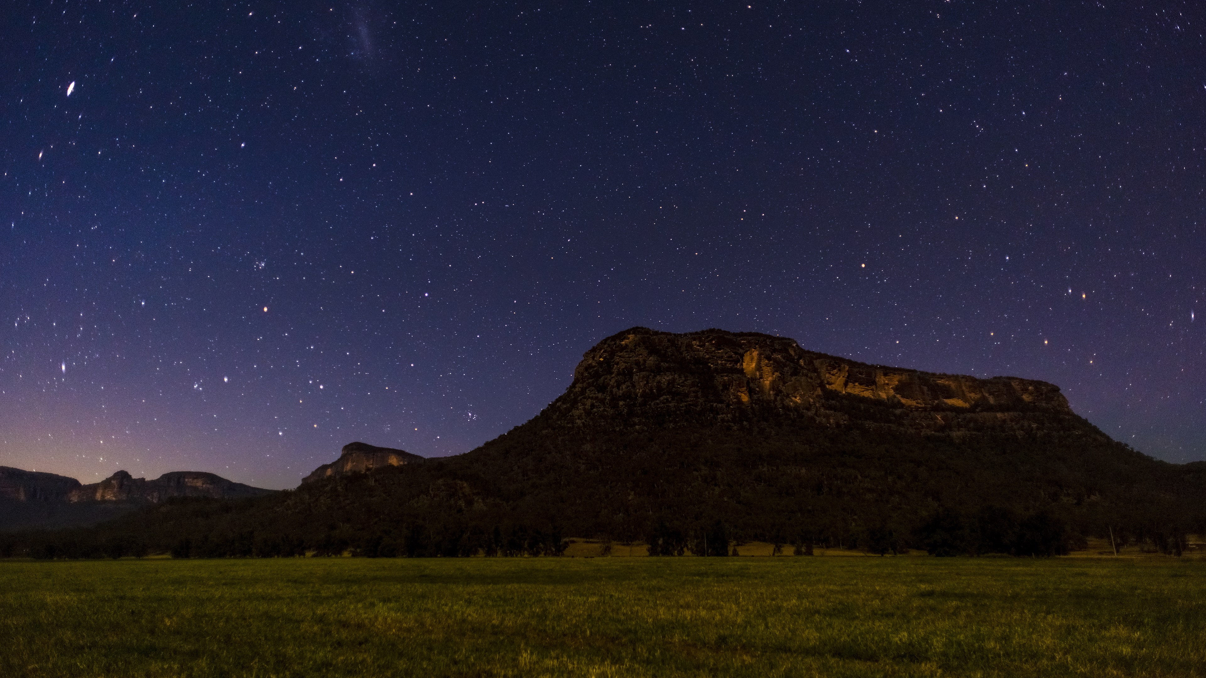 Starry night sky over mountains and a field HD Wallpaper