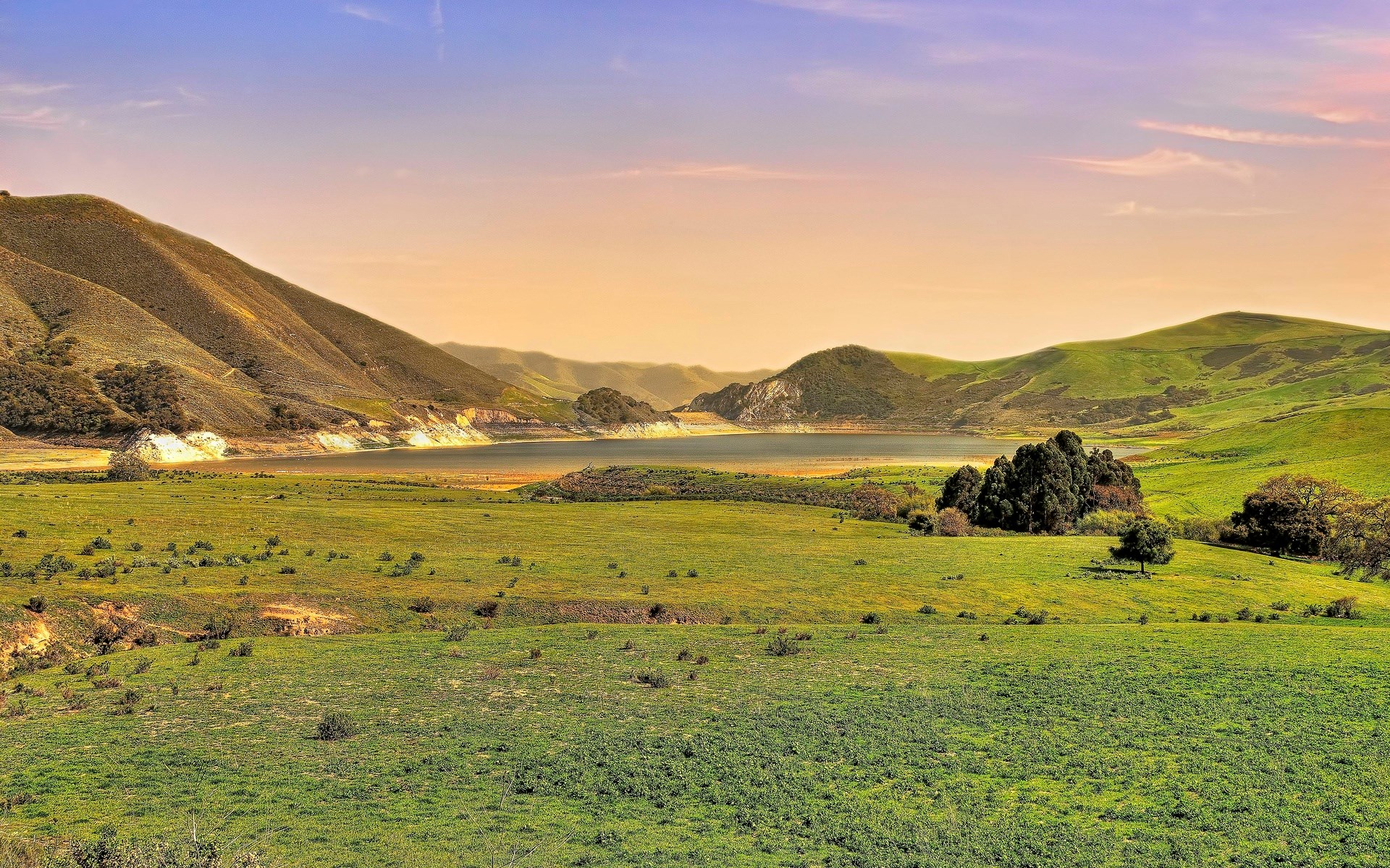 Rolling green hills and a lake under a sunset sky HD Wallpaper