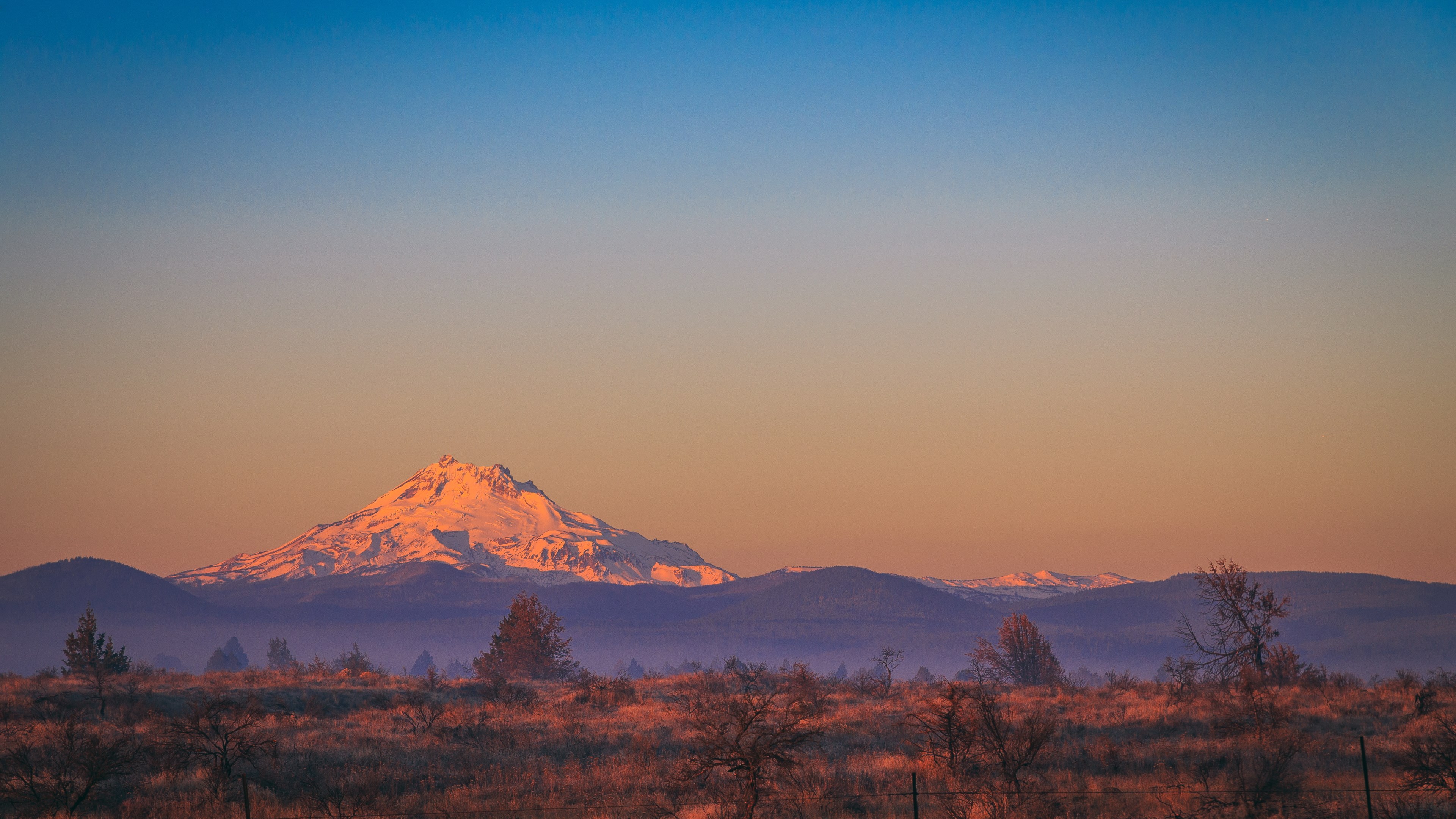 Snow-capped mountain at sunrise over dry landscape HD Wallpaper
