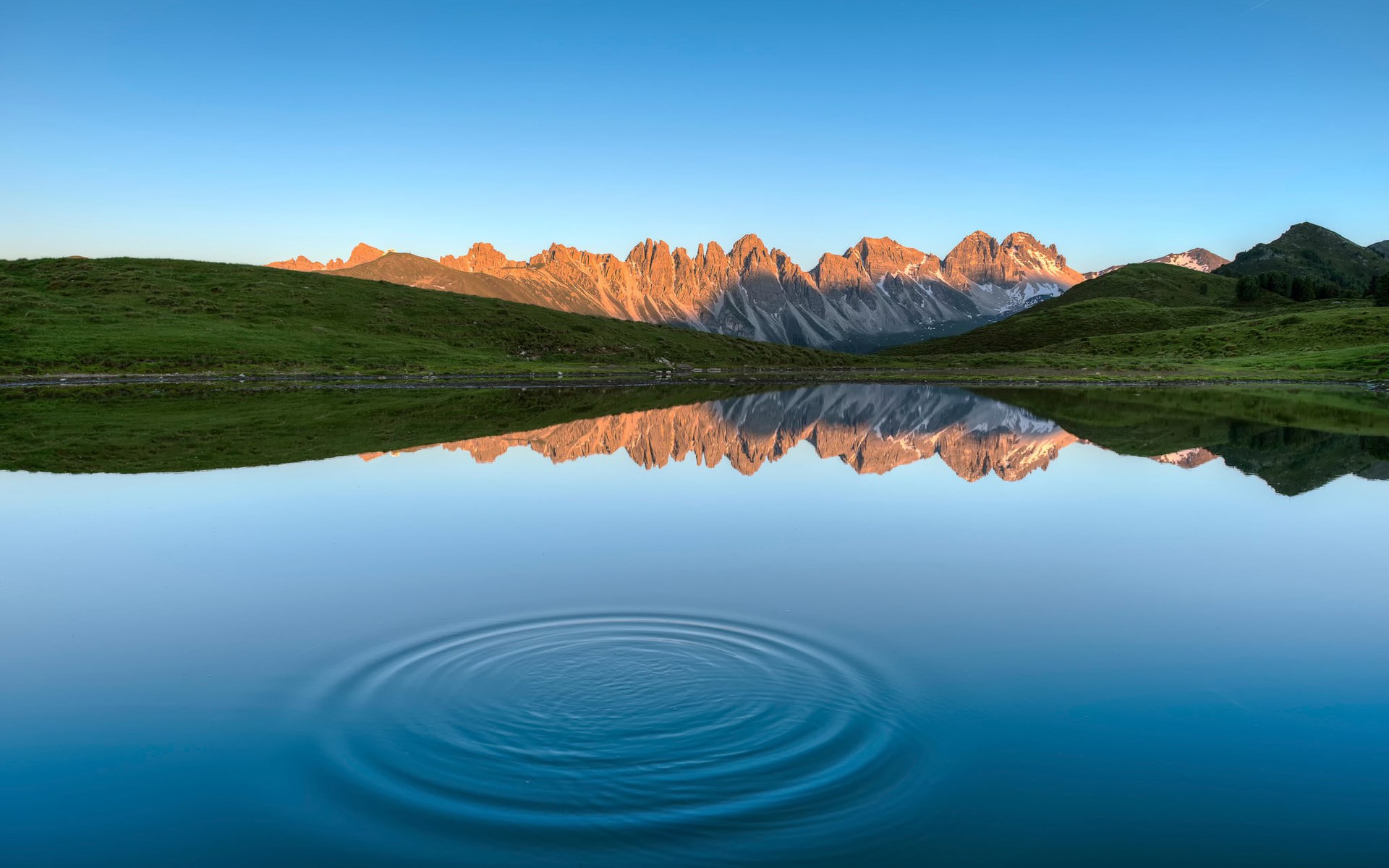 Mountain range reflected in a calm lake with ripples HD Wallpaper