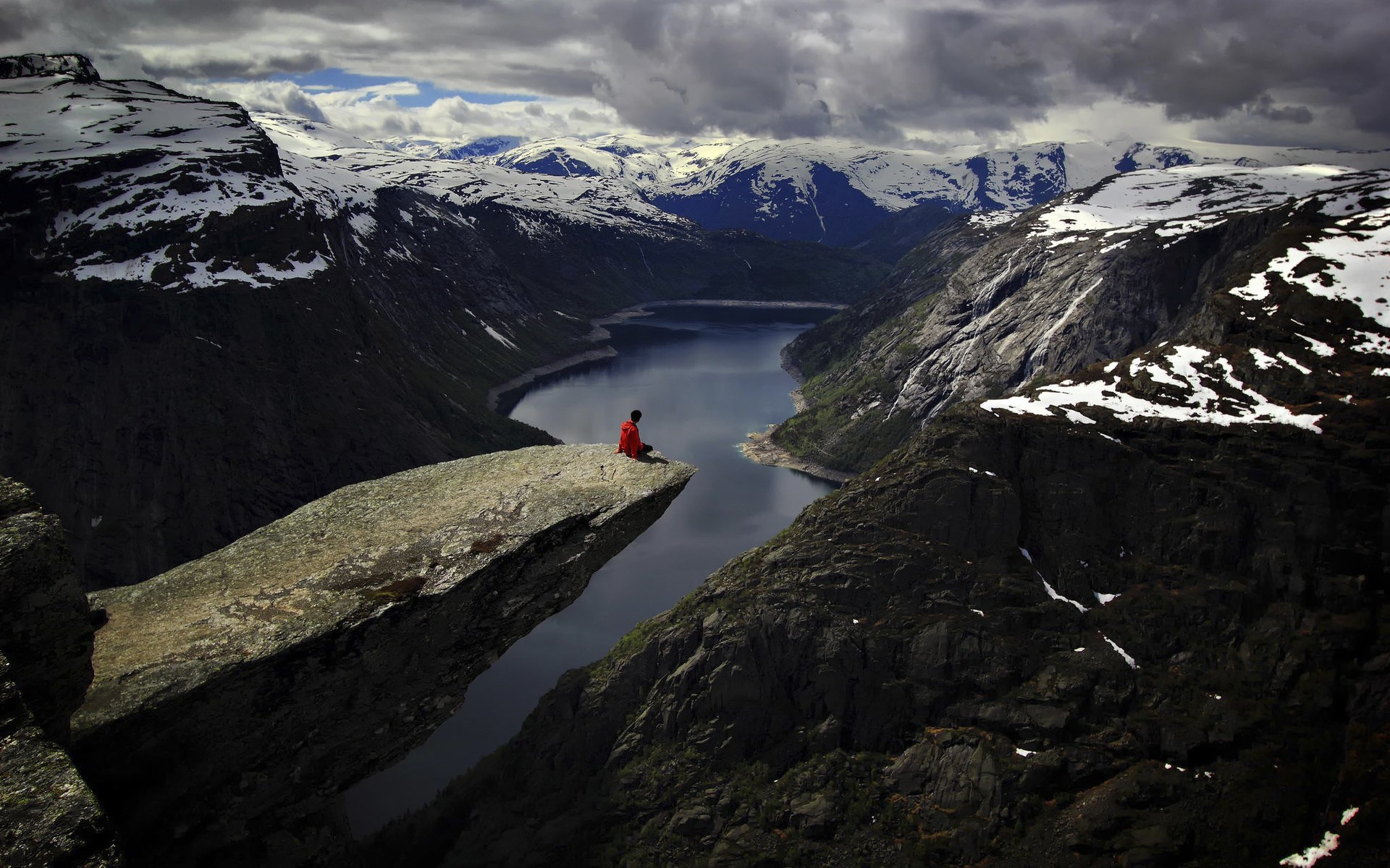 Person sitting on Trolltunga rock overlooking a fjord in Norway HD Wallpaper