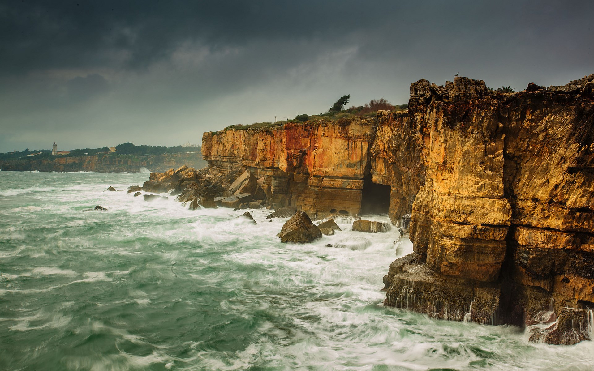 Waves crashing against rocky cliffs under a stormy sky HD Wallpaper