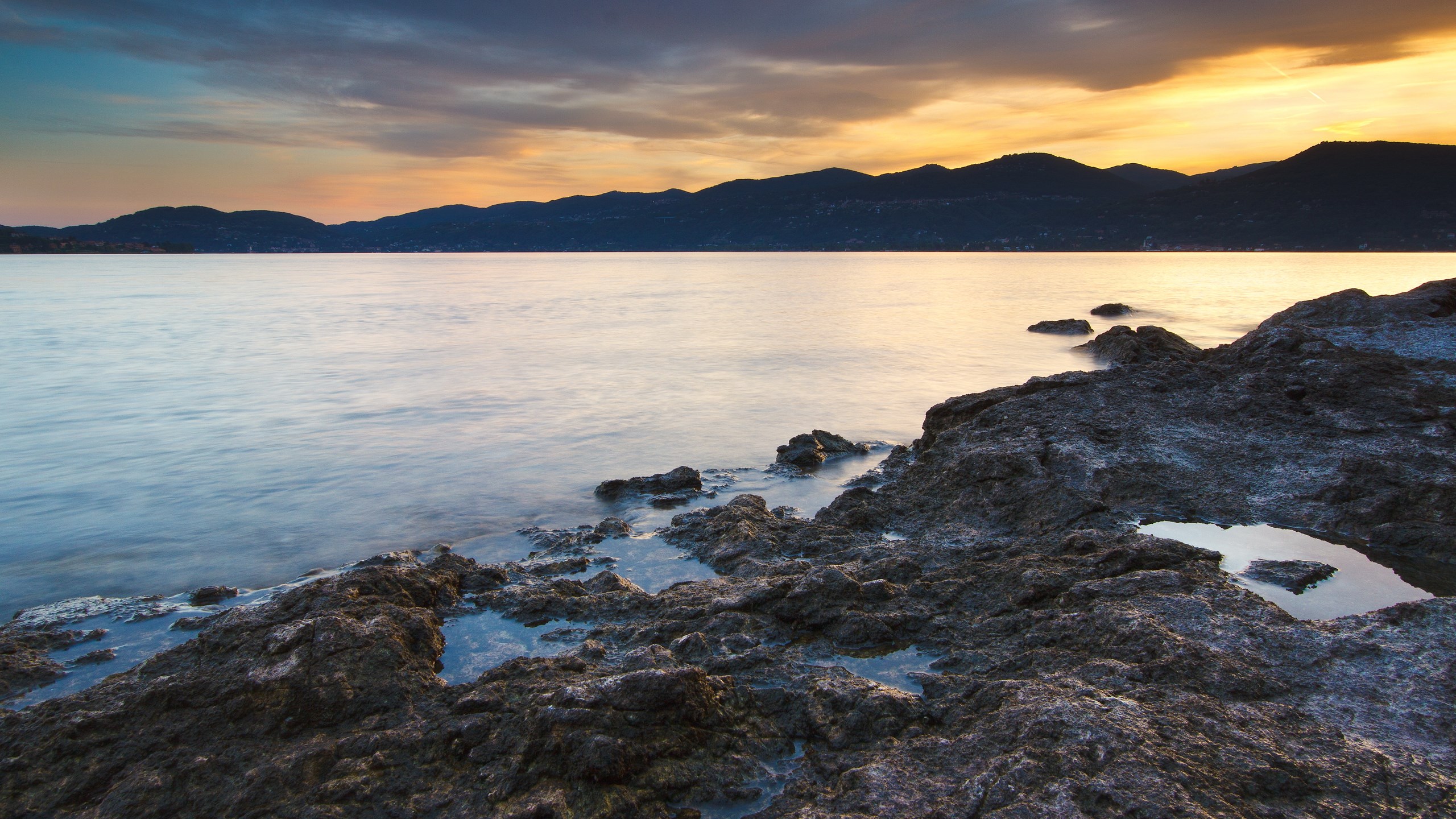 Rocky shore at sunset with mountains in the distance HD Wallpaper