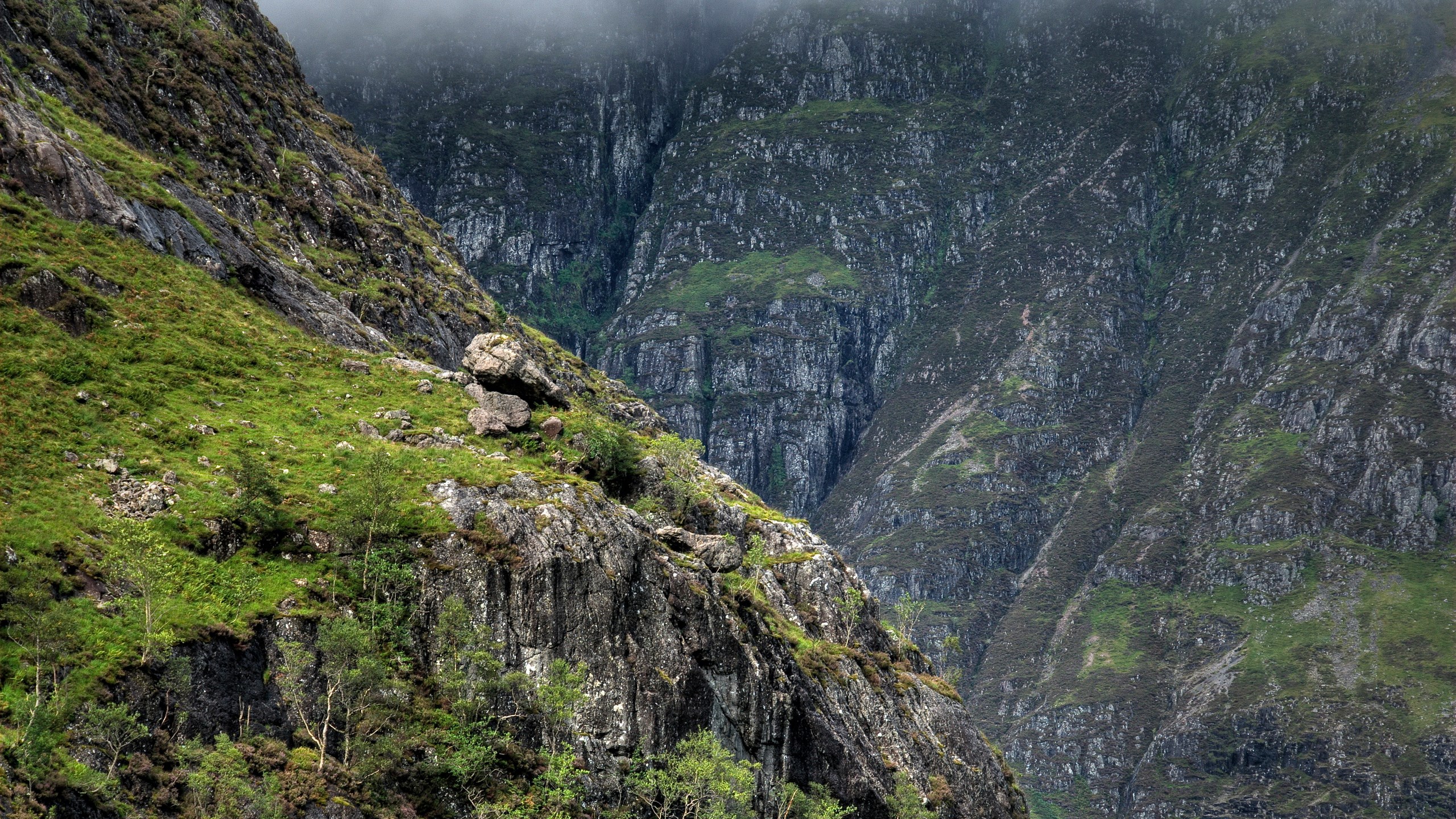 Steep, green, and rocky mountain slopes under a cloudy sky HD Wallpaper