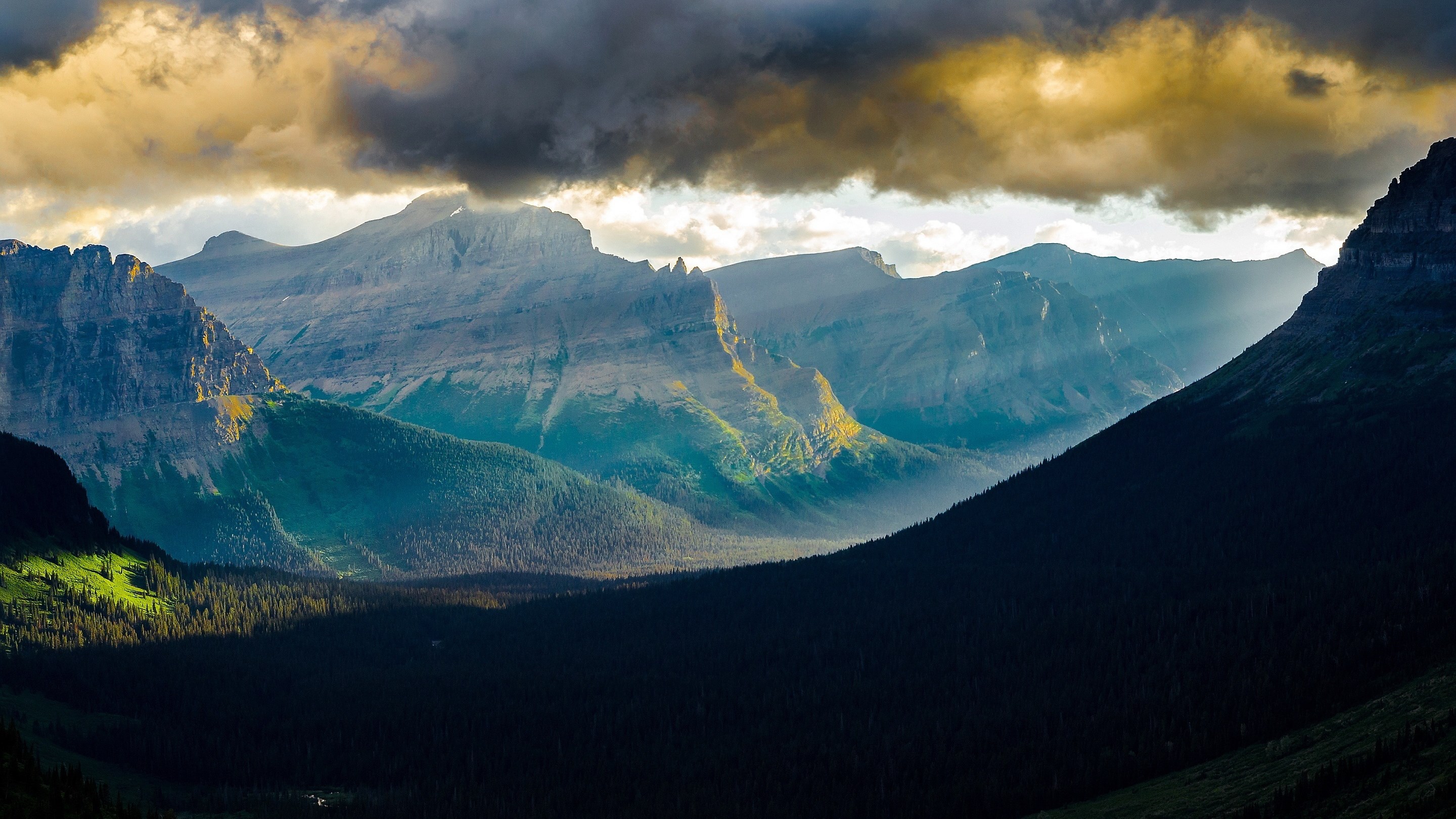 Sunlight beams through clouds onto mountains and forest HD Wallpaper