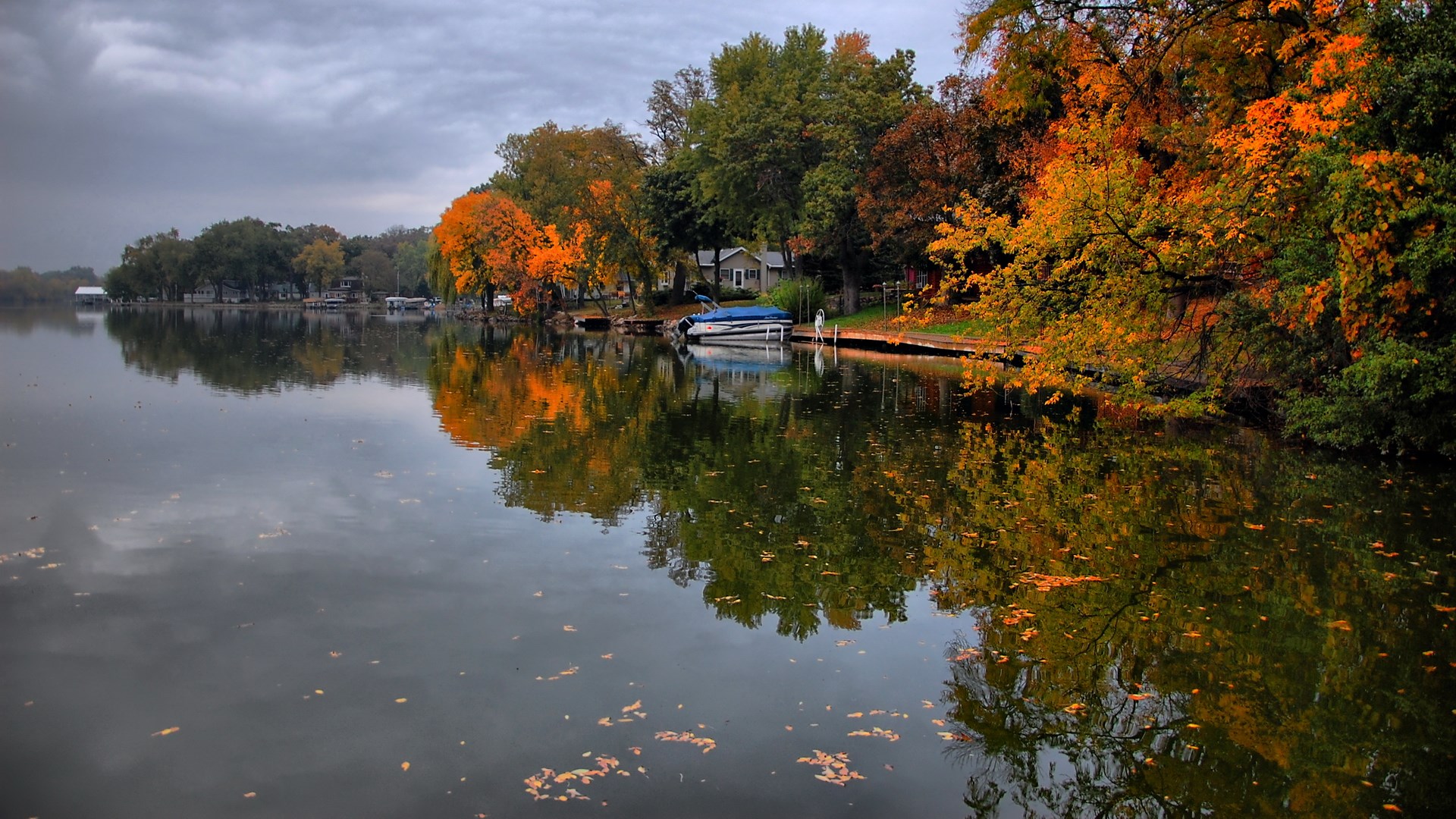 Autumn trees reflecting in a calm lake with a boat HD Wallpaper