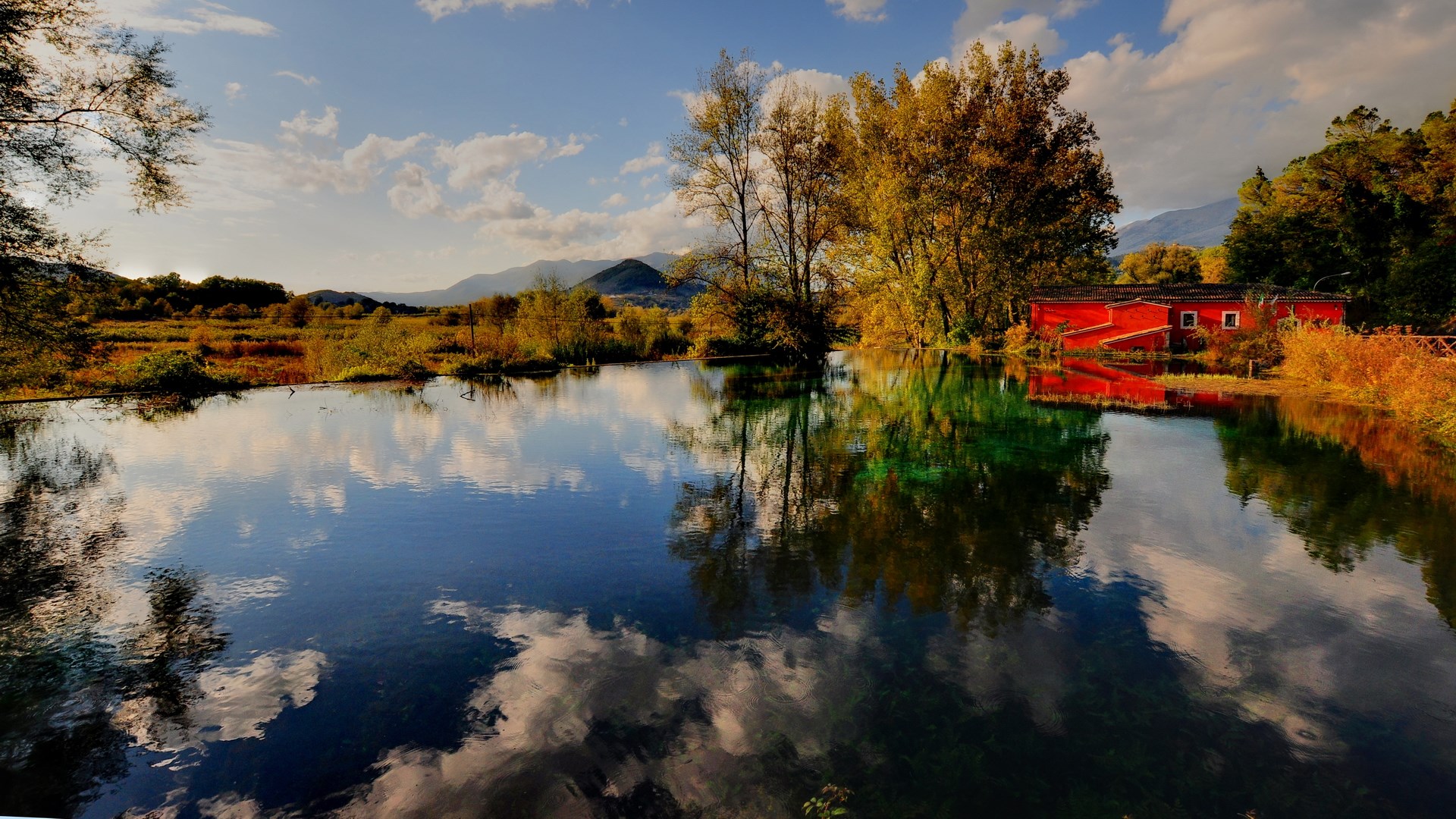 Red building reflected in a calm lake with trees HD Wallpaper