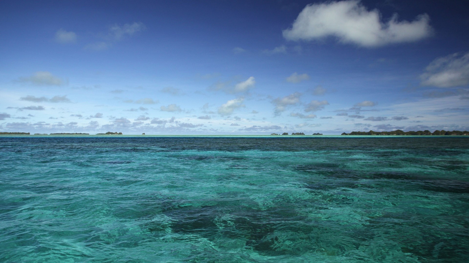 Turquoise ocean water with islands on the horizon under a blue sky HD Wallpaper
