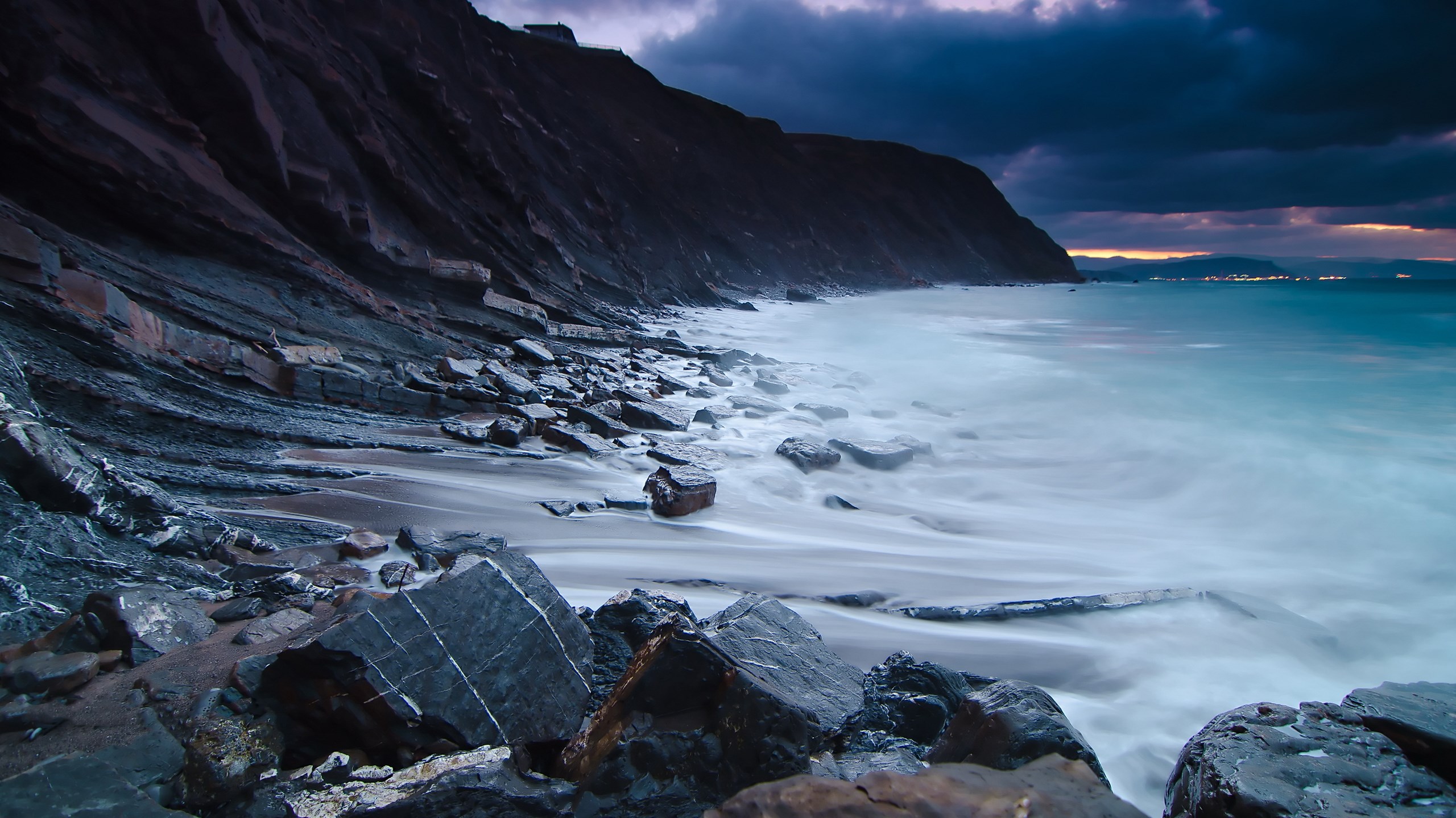 Rocky coastline with waves crashing at dusk HD Wallpaper