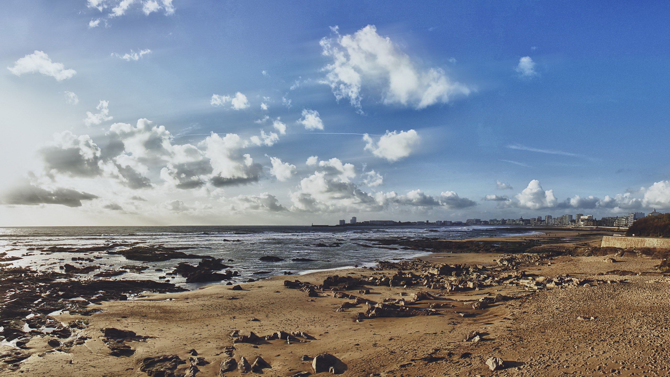 Rocky beach with city skyline and cloudy sky HD Wallpaper