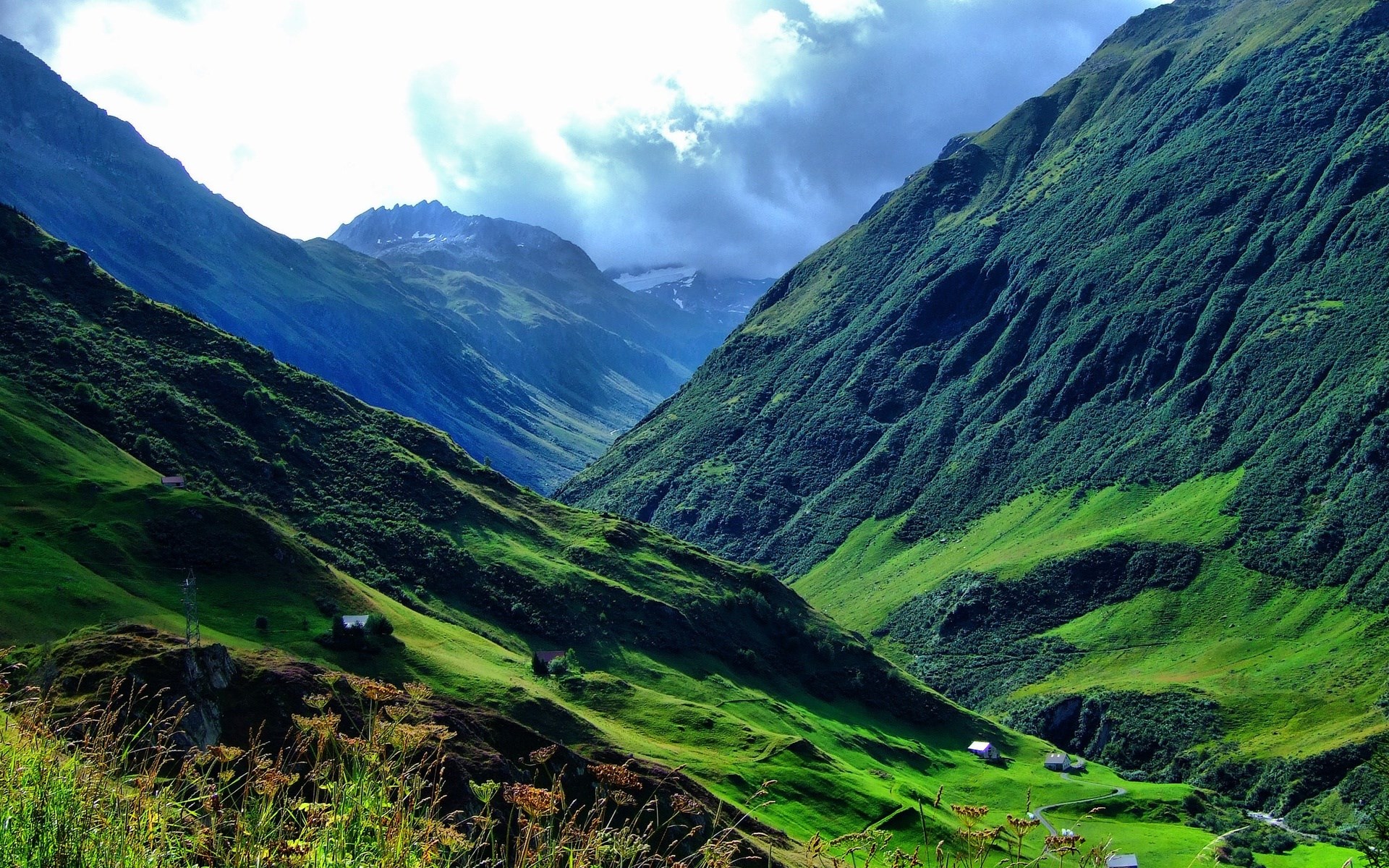 Green mountain valley with scattered houses and cloudy sky HD Wallpaper