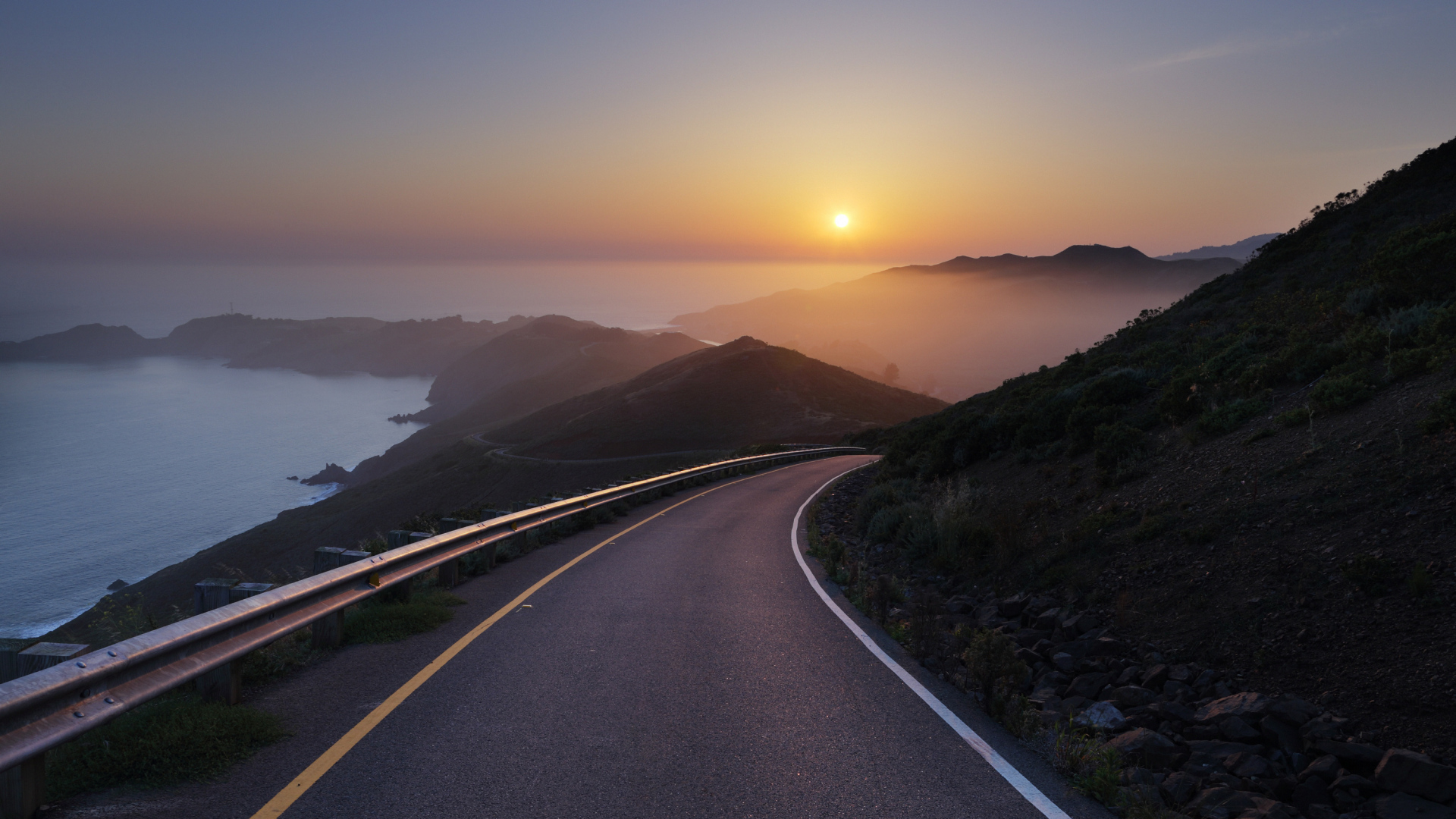 Road winding through hills by the sea at sunset HD Wallpaper