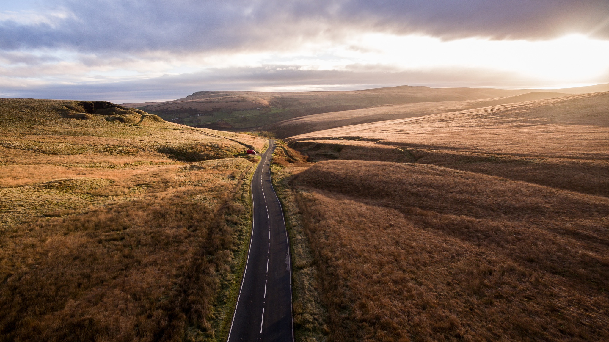 Road through a grassy landscape under a cloudy sky HD Wallpaper