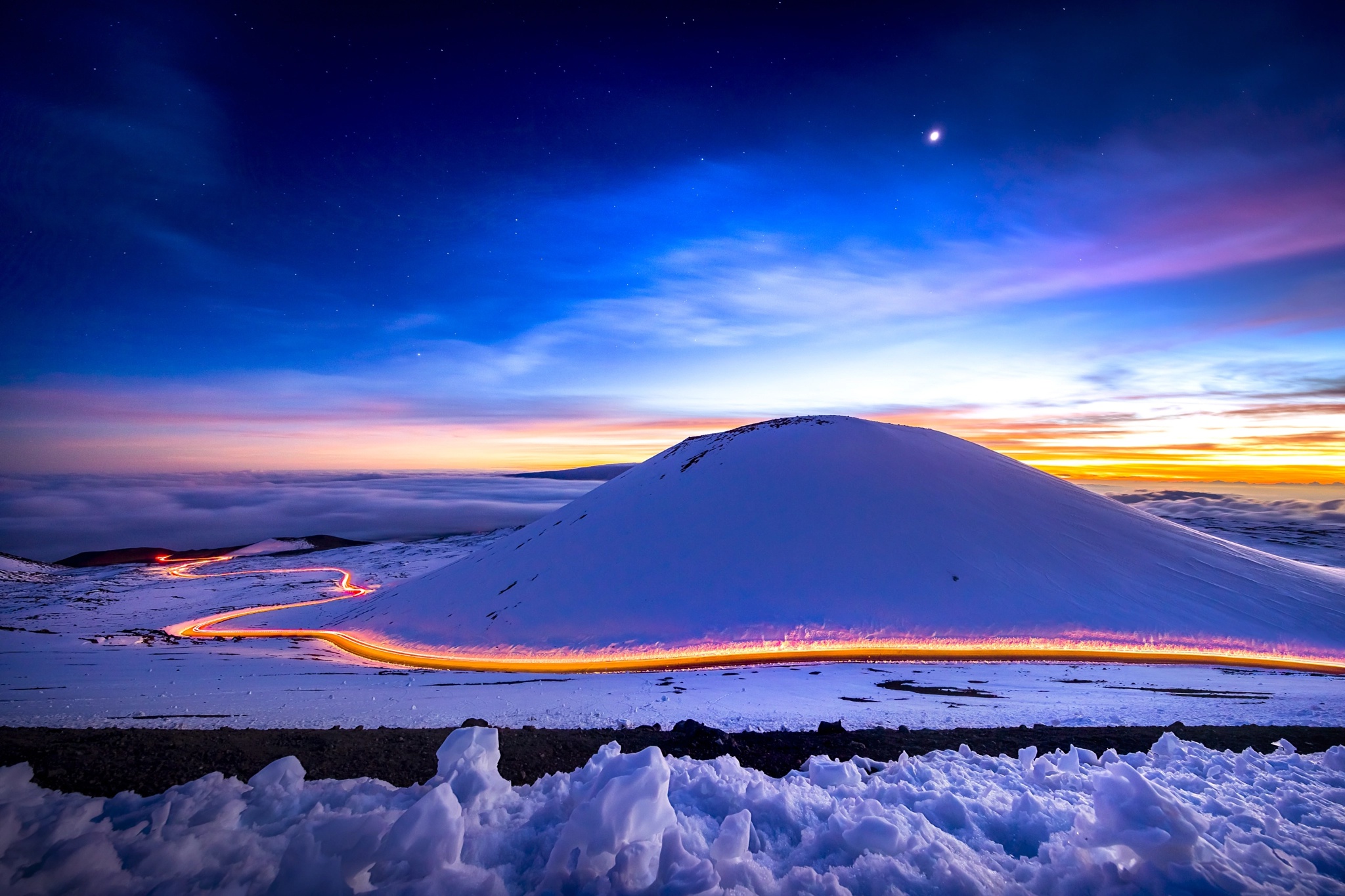 Snowy mountain road with light trails at sunset HD Wallpaper