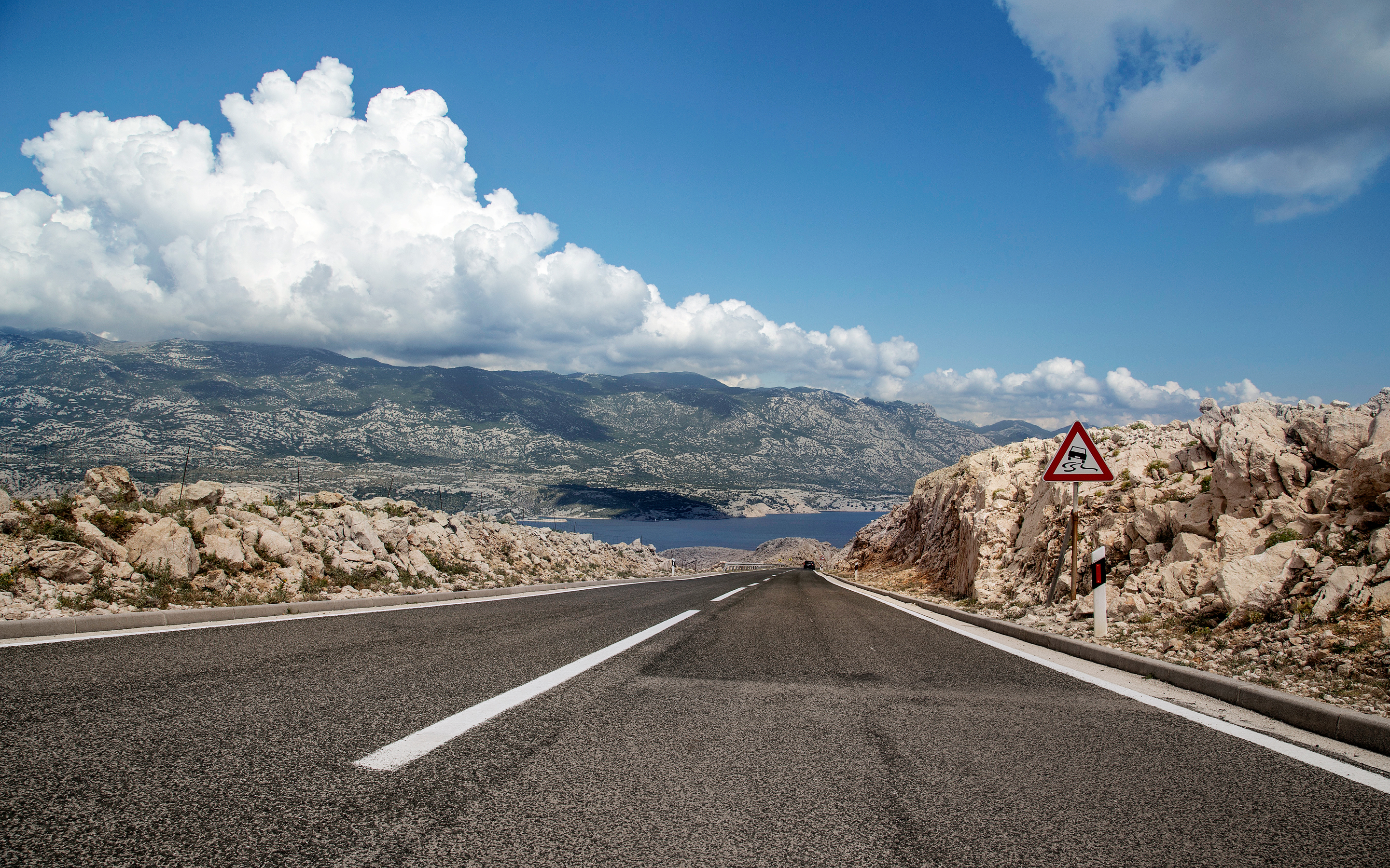 Road leading to mountains and sea under clouds HD Wallpaper