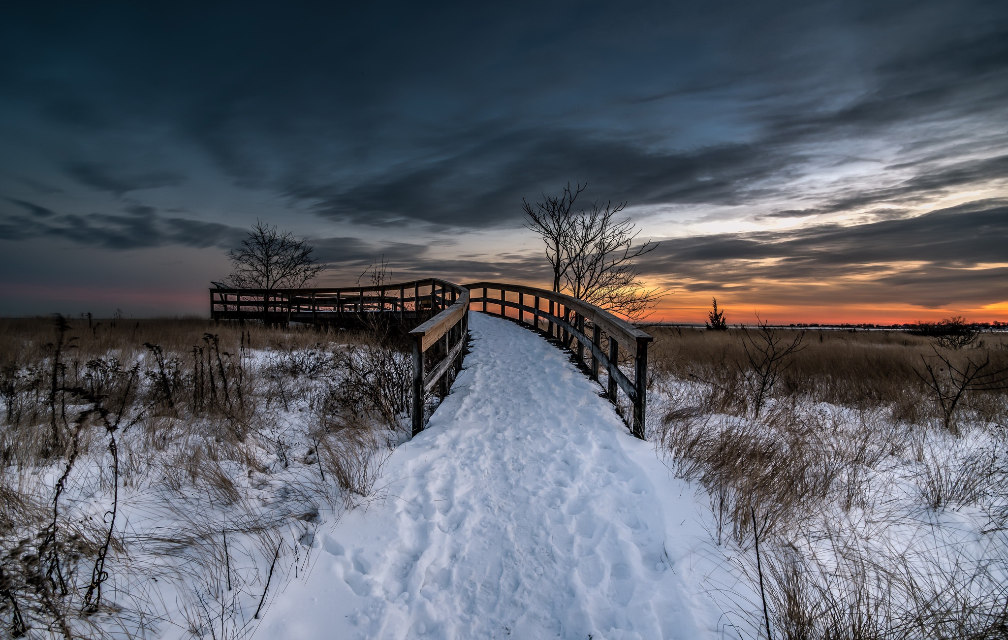 Snow-covered boardwalk through a winter landscape at sunset HD Wallpaper