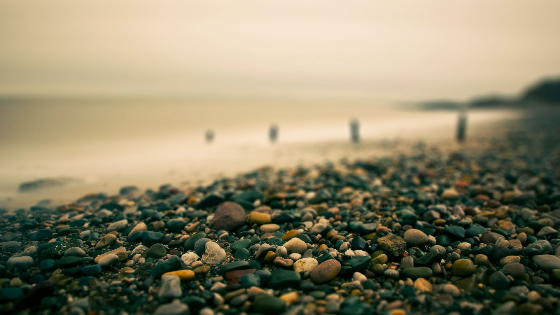 Pebble beach with ocean and wooden posts HD Wallpaper