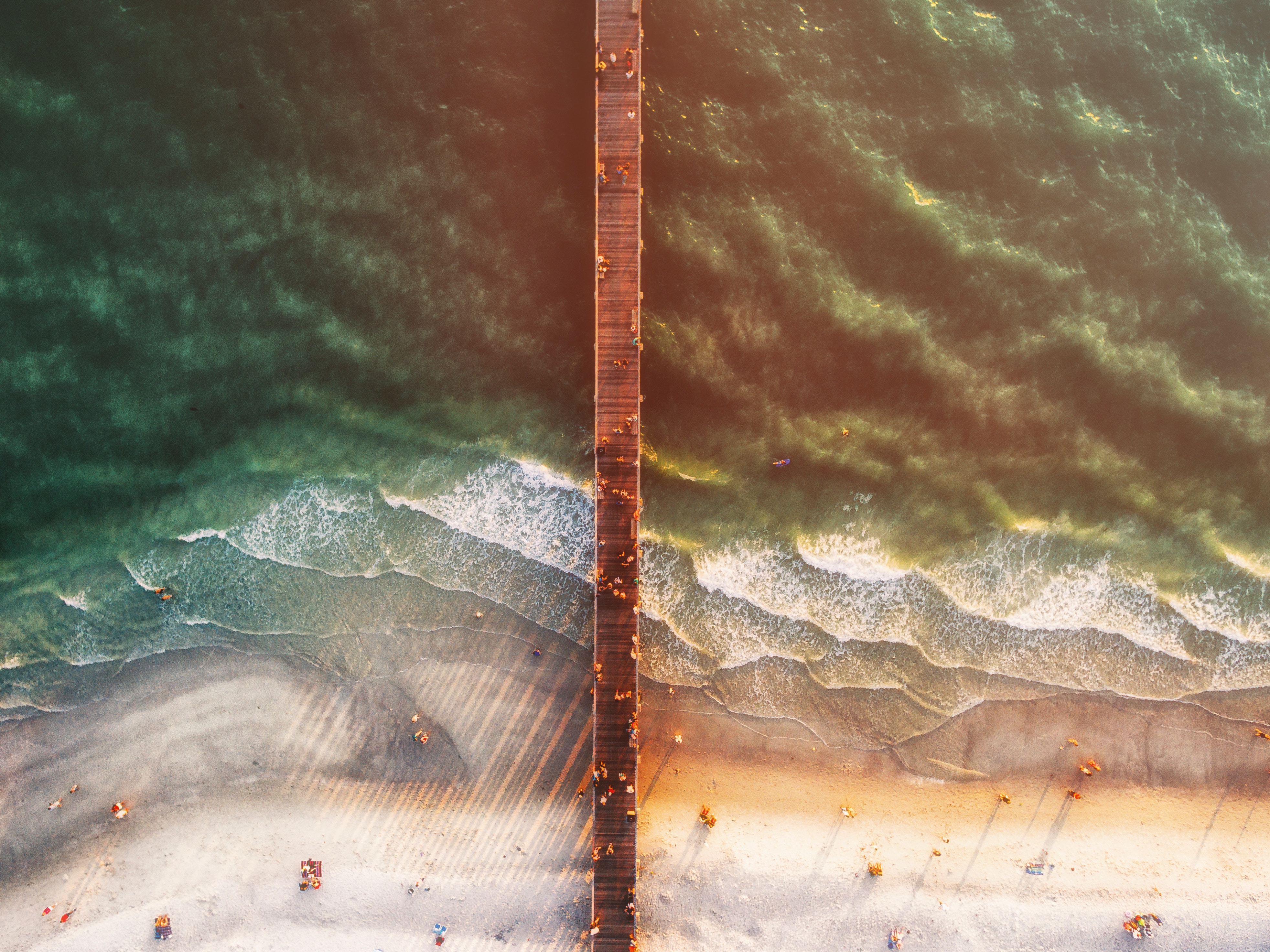 Aerial view of a pier extending over the ocean at a beach HD Wallpaper