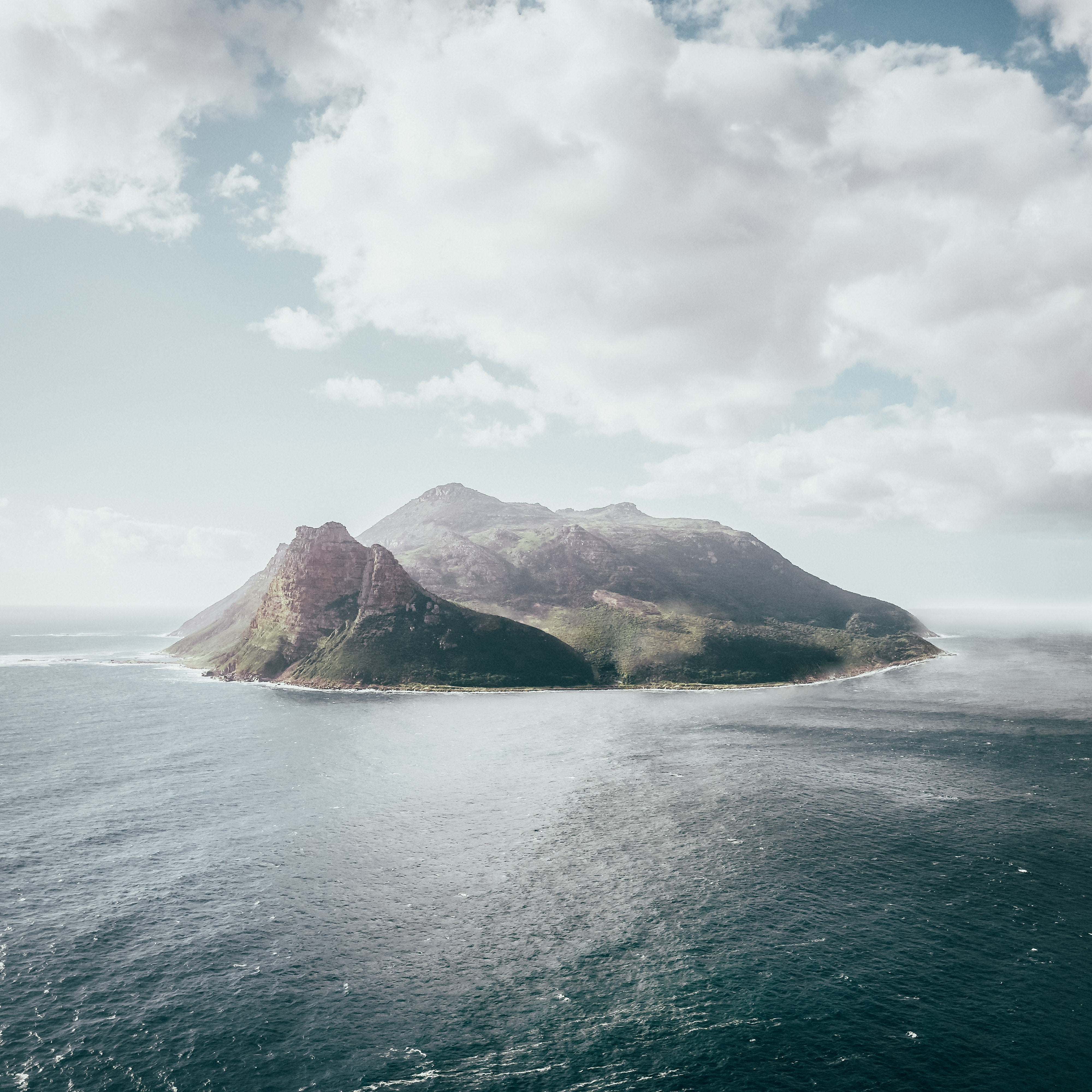 Island mountains surrounded by the ocean under a cloudy sky HD Wallpaper