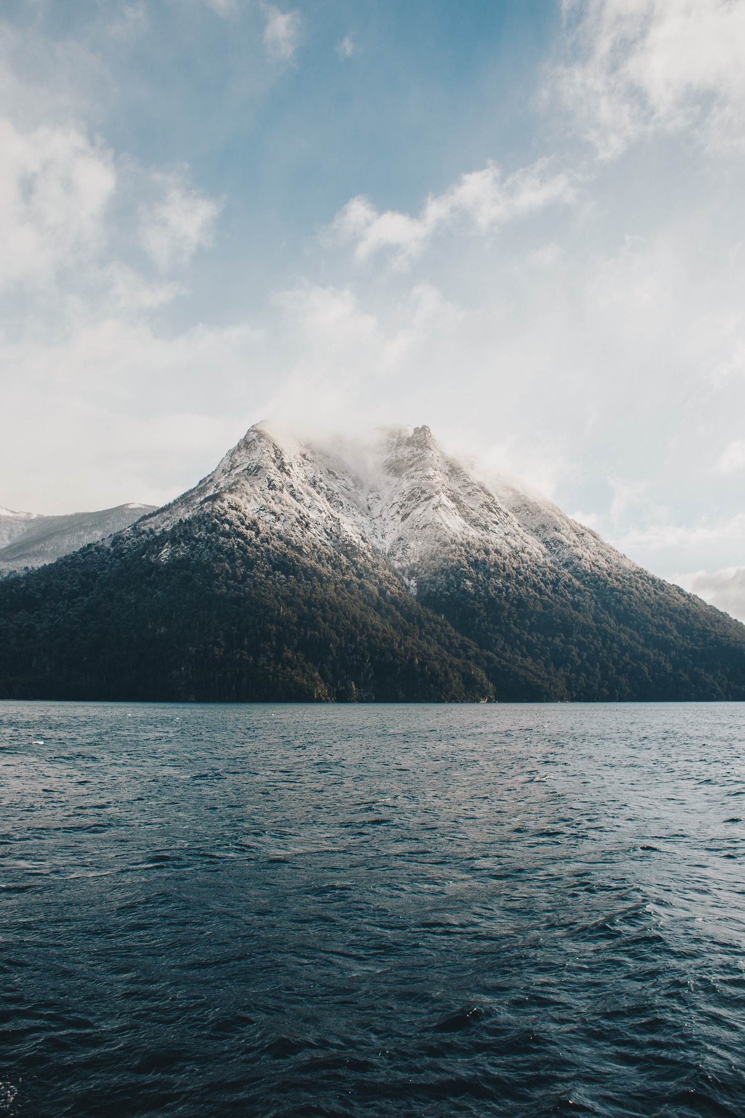Snow-capped mountain overlooking a dark blue lake HD Wallpaper