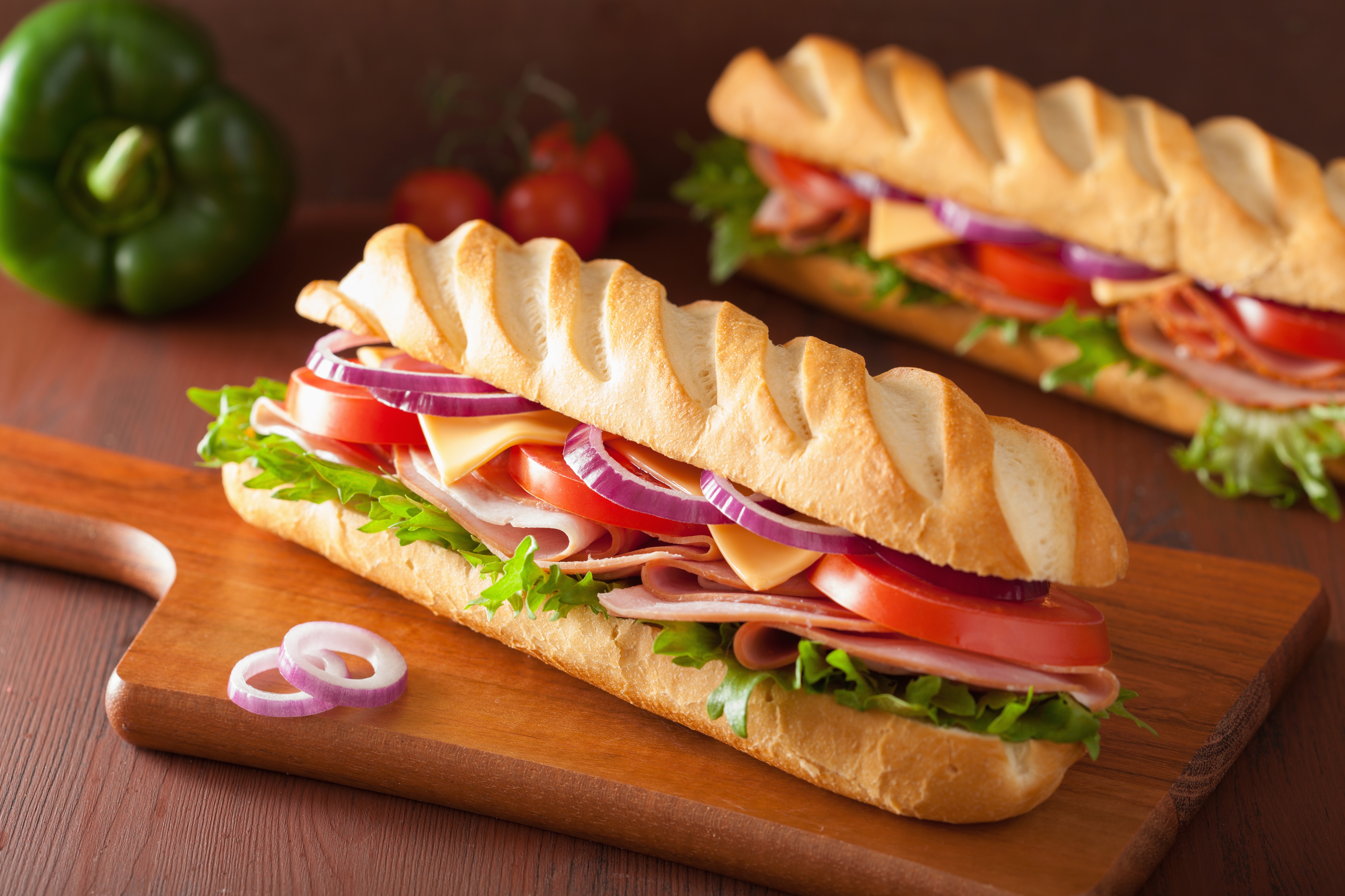 Two gourmet sandwiches on a wooden board with vegetables HD Wallpaper