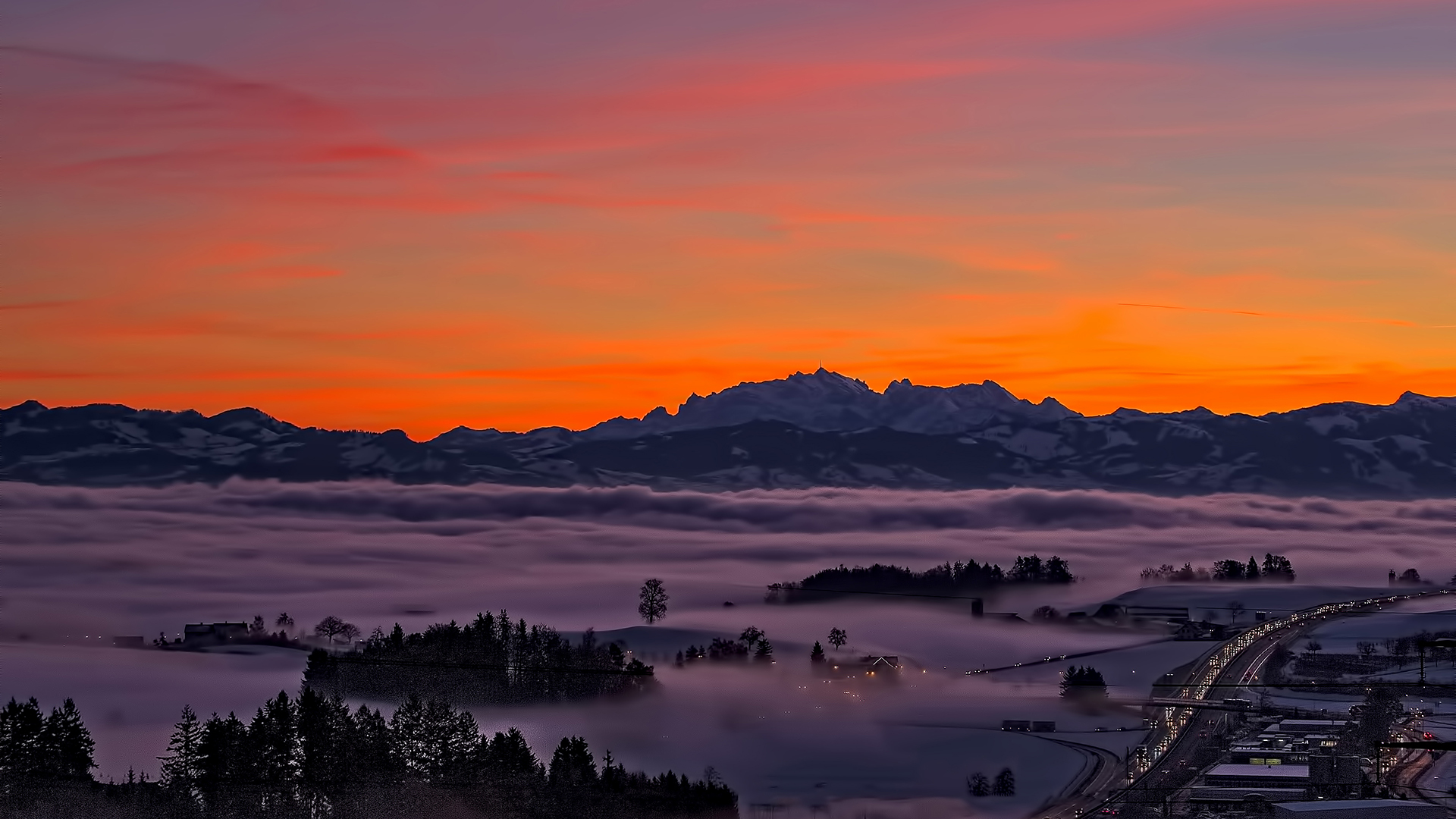Mountains over fog at sunset with highway HD Wallpaper