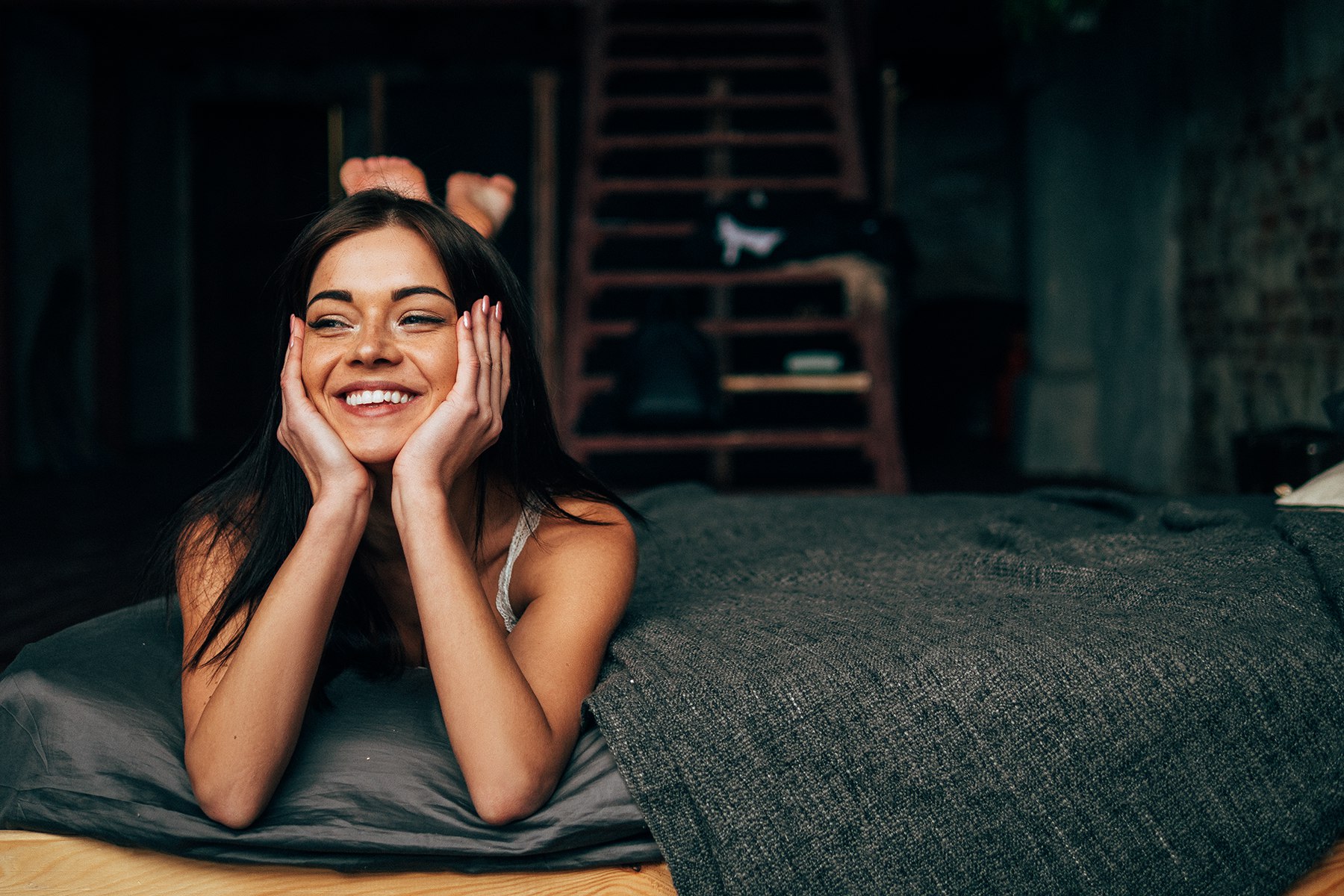 Smiling woman lying on bed with hands on cheeks HD Wallpaper