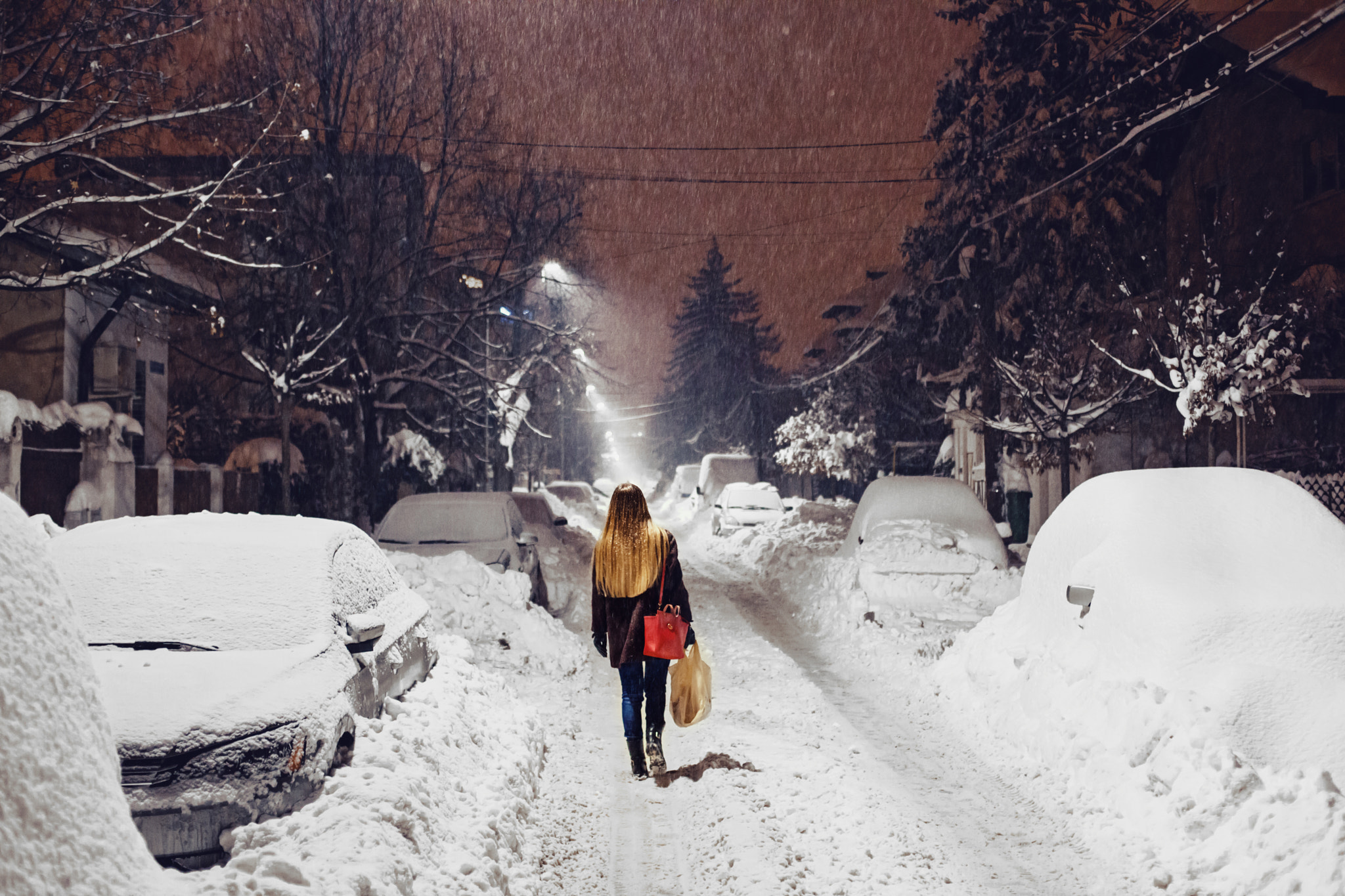 Woman walking down a snowy street at night HD Wallpaper