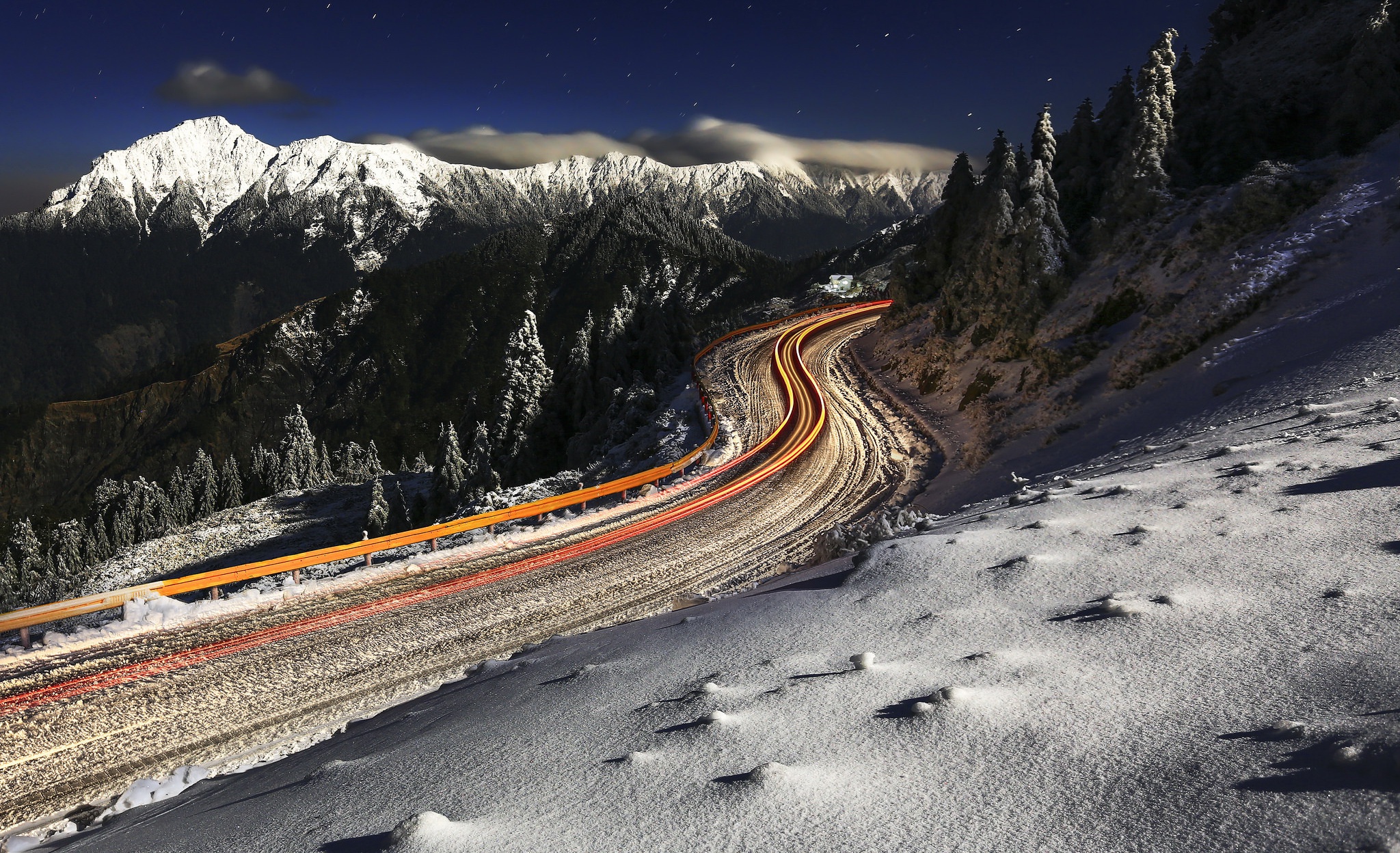 Snowy mountain road with car light trails at night HD Wallpaper