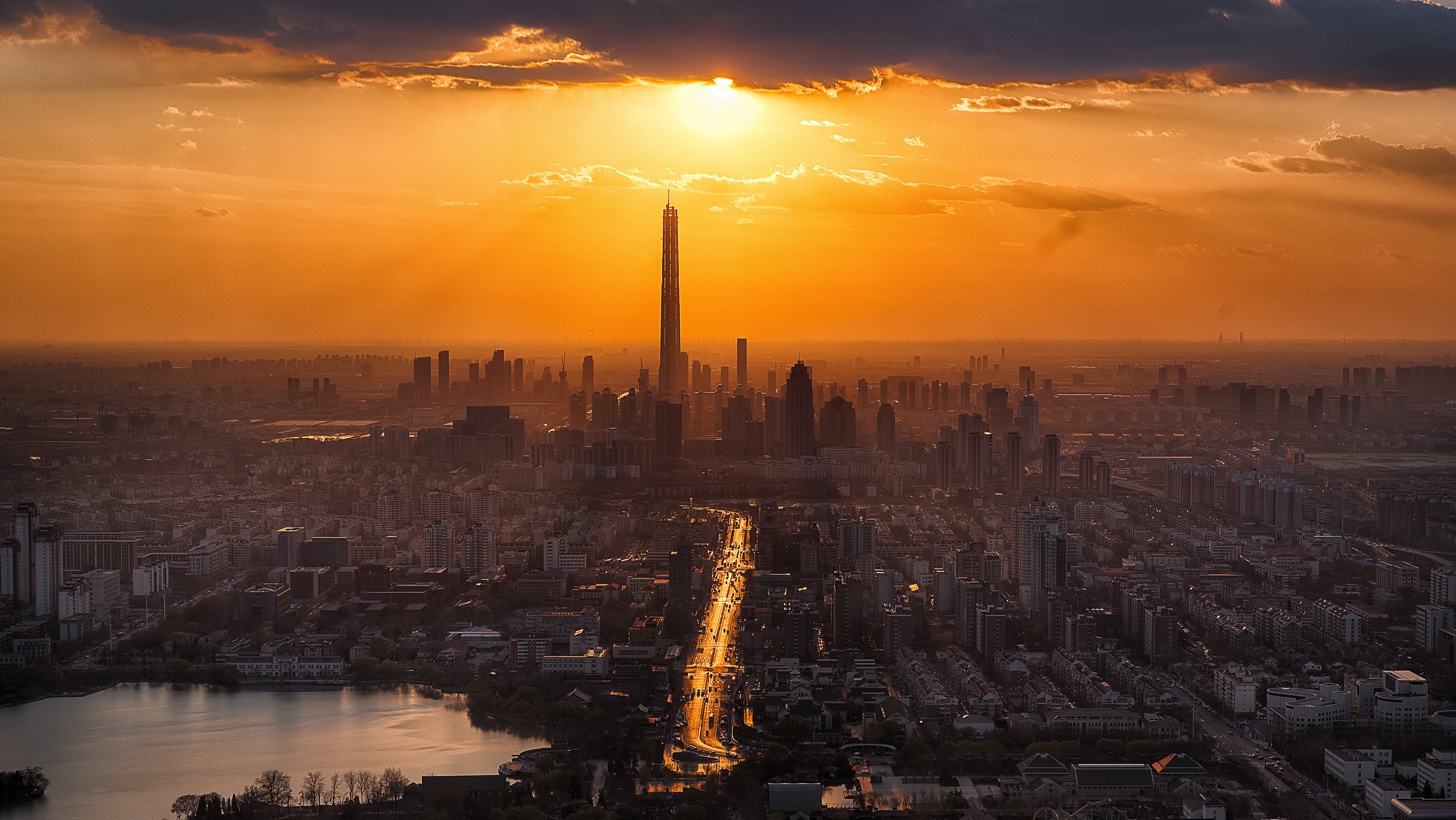Cityscape at sunset with a tall skyscraper and a lake HD Wallpaper