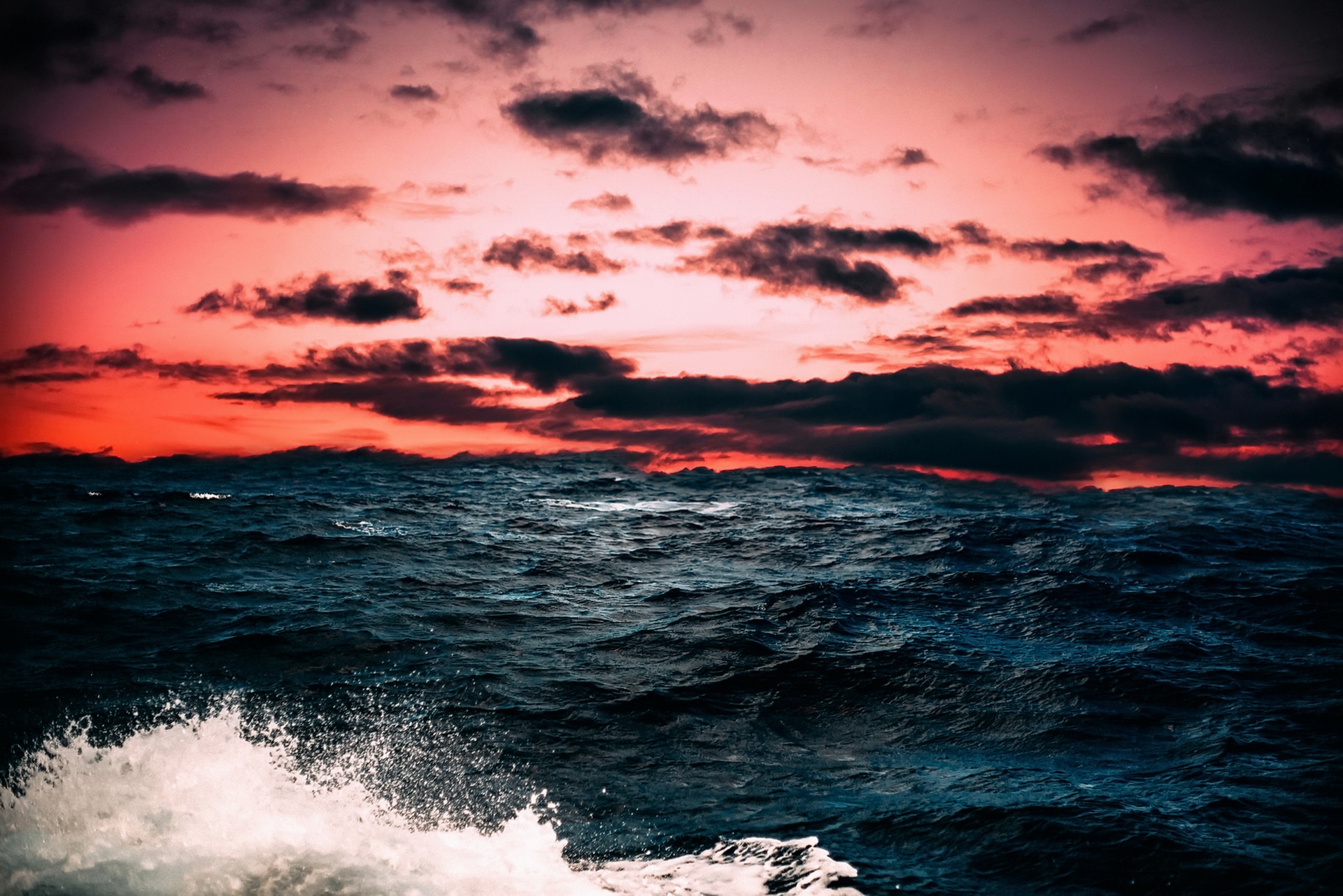 Dark ocean waves under a dramatic sunset sky HD Wallpaper