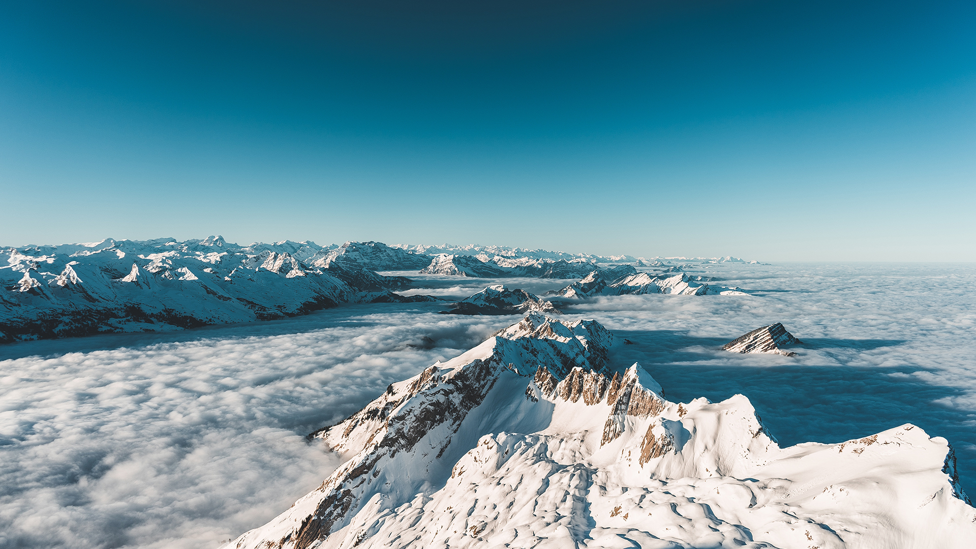 Snow-capped mountains above clouds under a clear blue sky HD Wallpaper